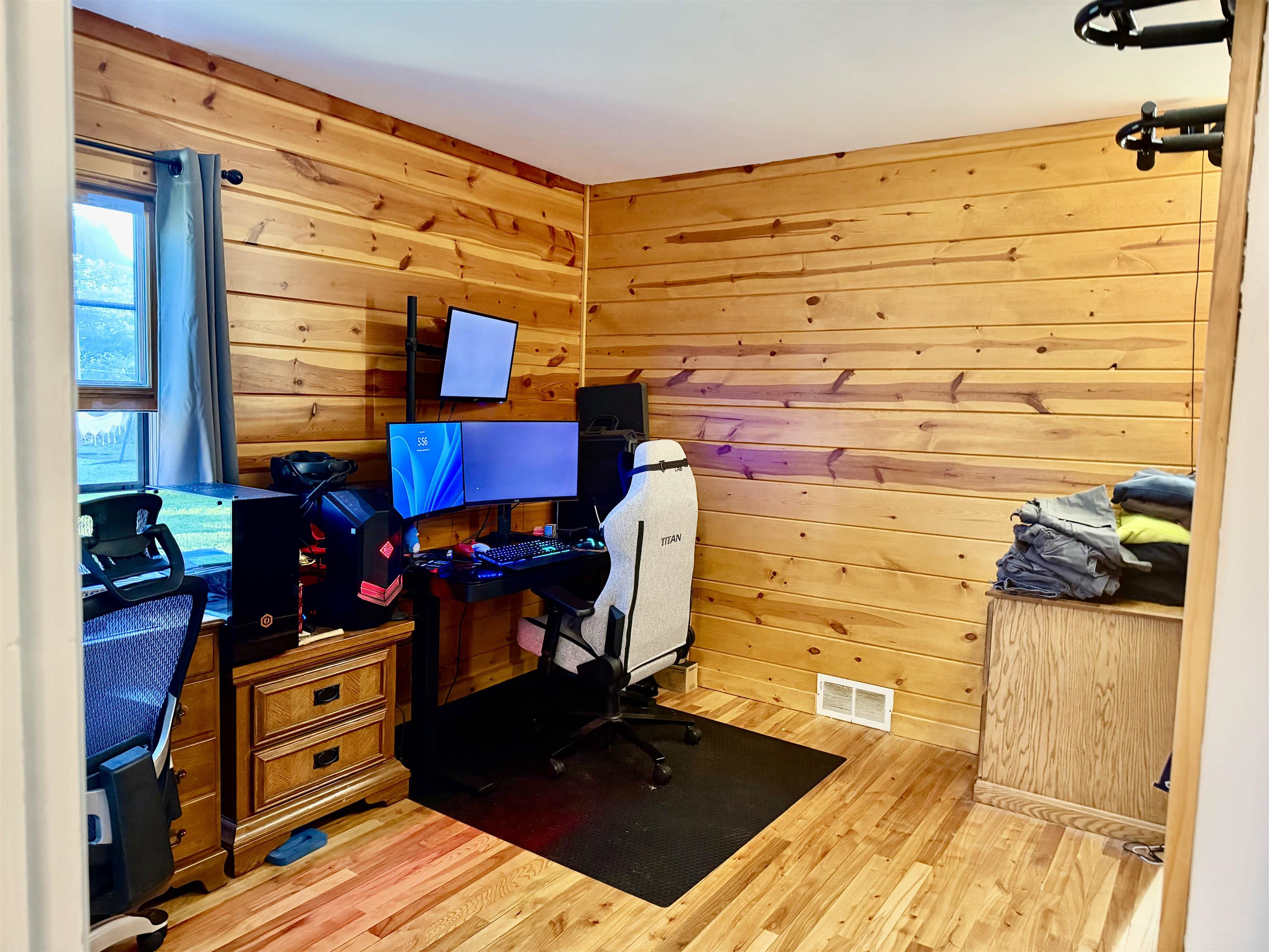 Pine-paneled home office with a multi-monitor gaming desk and white chair.
