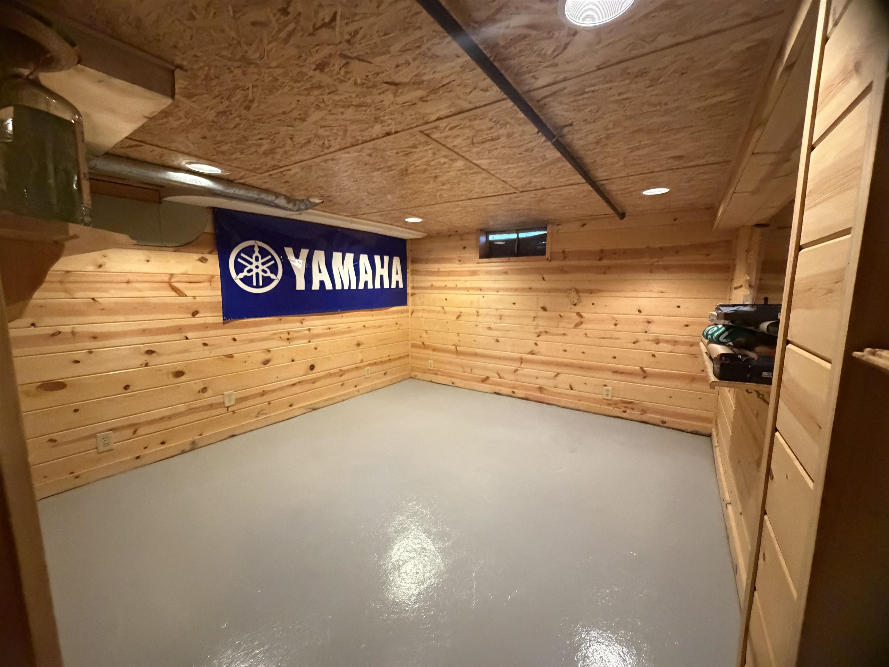 Basement with wood-paneled walls, a gray floor, and a blue Yamaha banner.