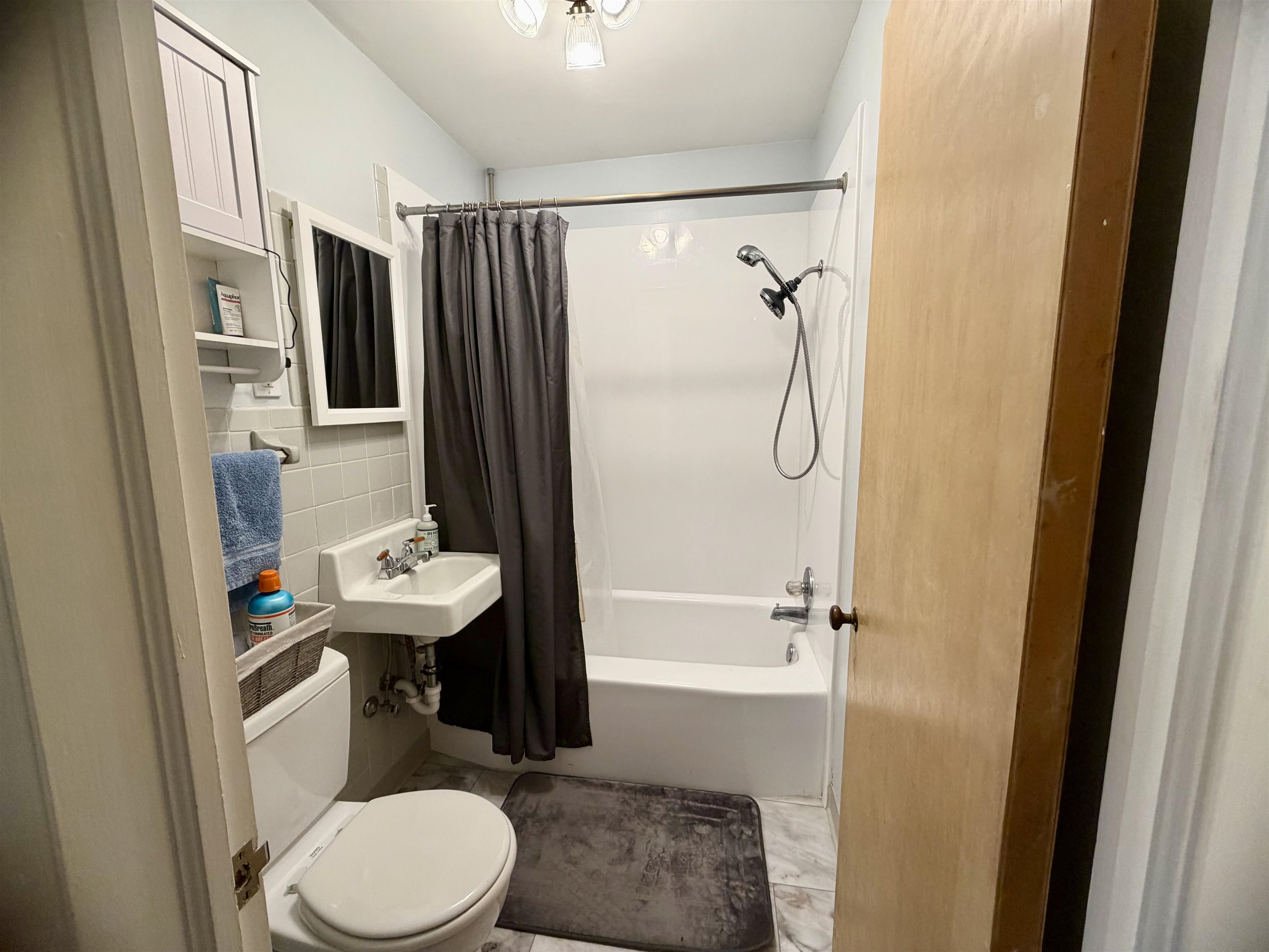 Bathroom with a white tub, dark shower curtain, wall-mounted sink, and toilet.