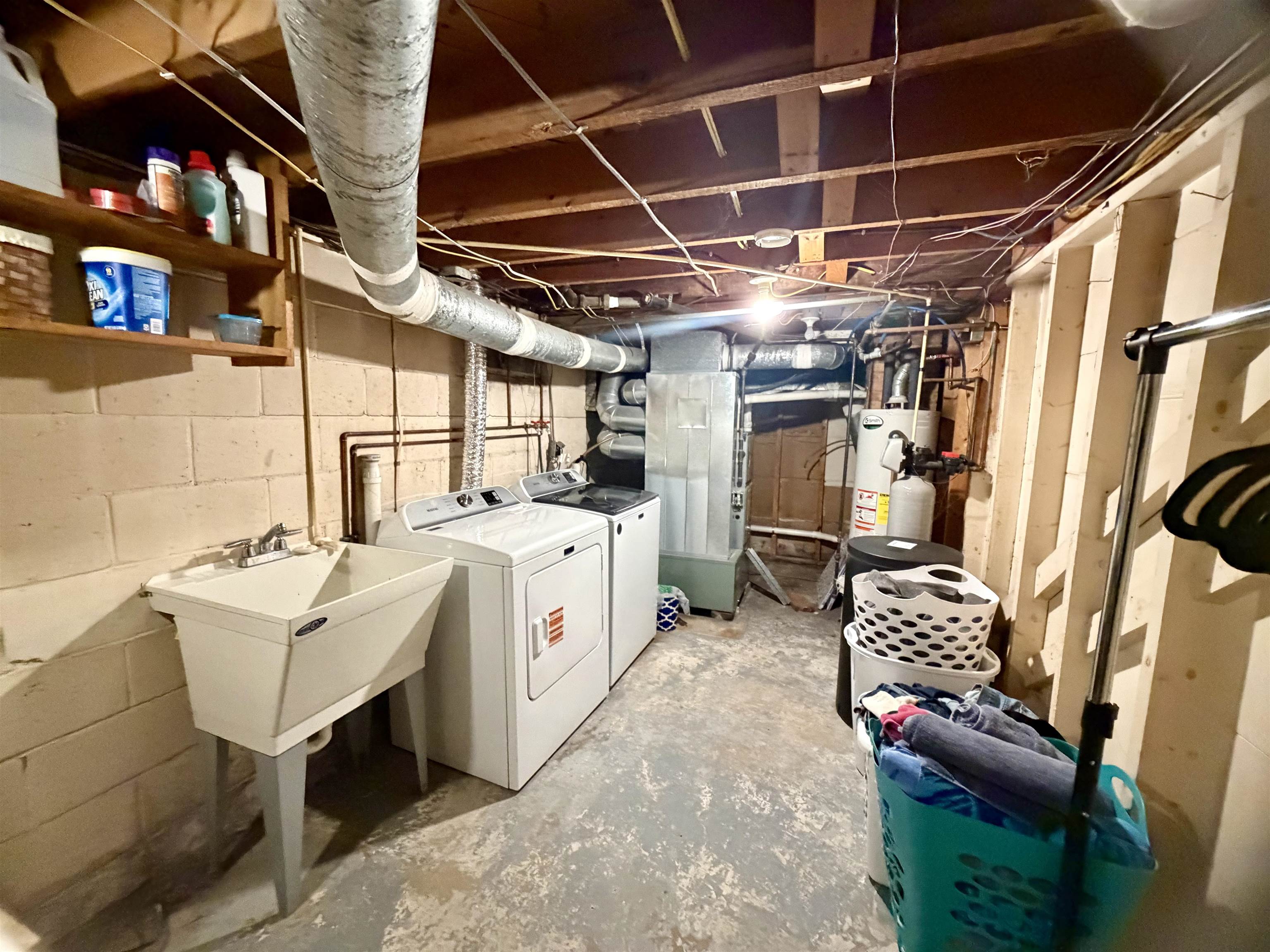 Basement laundry area with a utility sink, washer, dryer, and exposed ductwork.