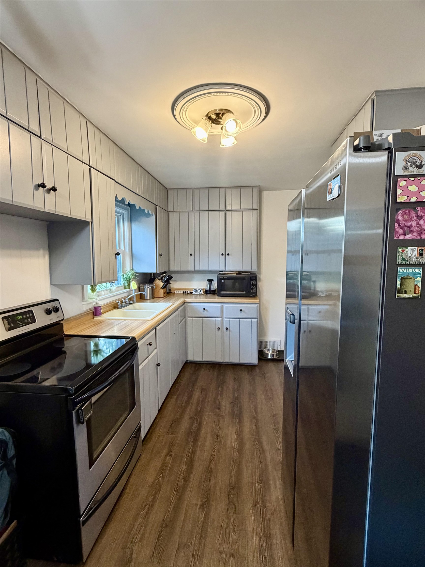 Galley kitchen with white cabinets, a double sink, black range, and stainless steel refrigerator.