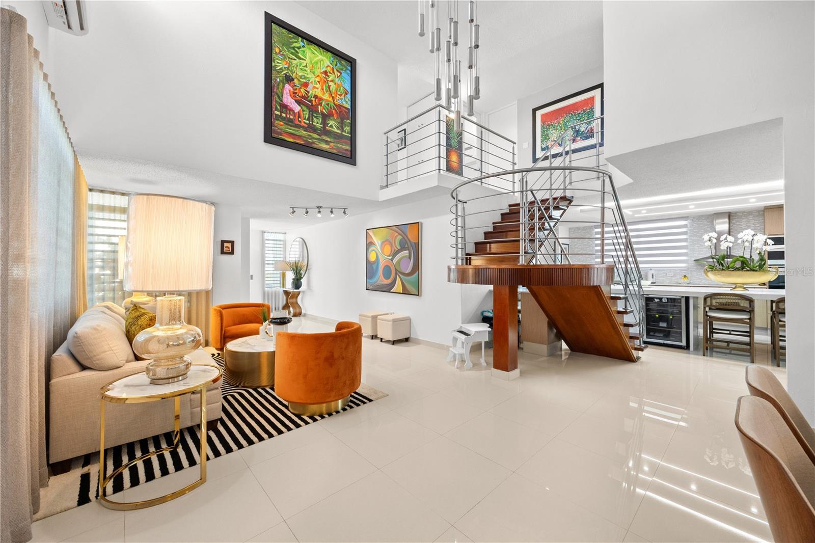 Open-plan living room with a curved wooden staircase, double-height ceiling, and orange accent chairs.