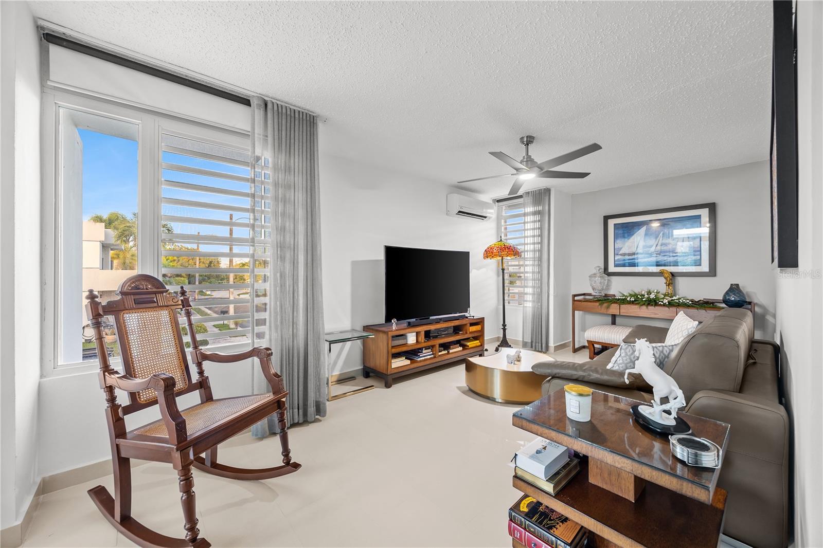 Living room with a wooden rocking chair, large windows, TV, and gray sofa.