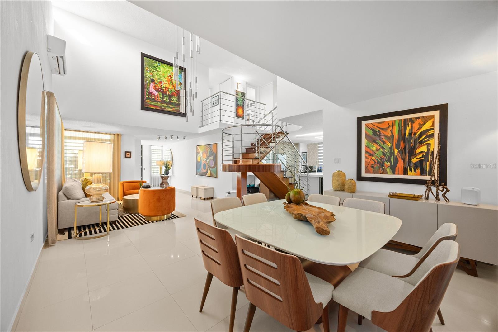 Open-plan living and dining room with colorful artwork and a wood-and-metal staircase.