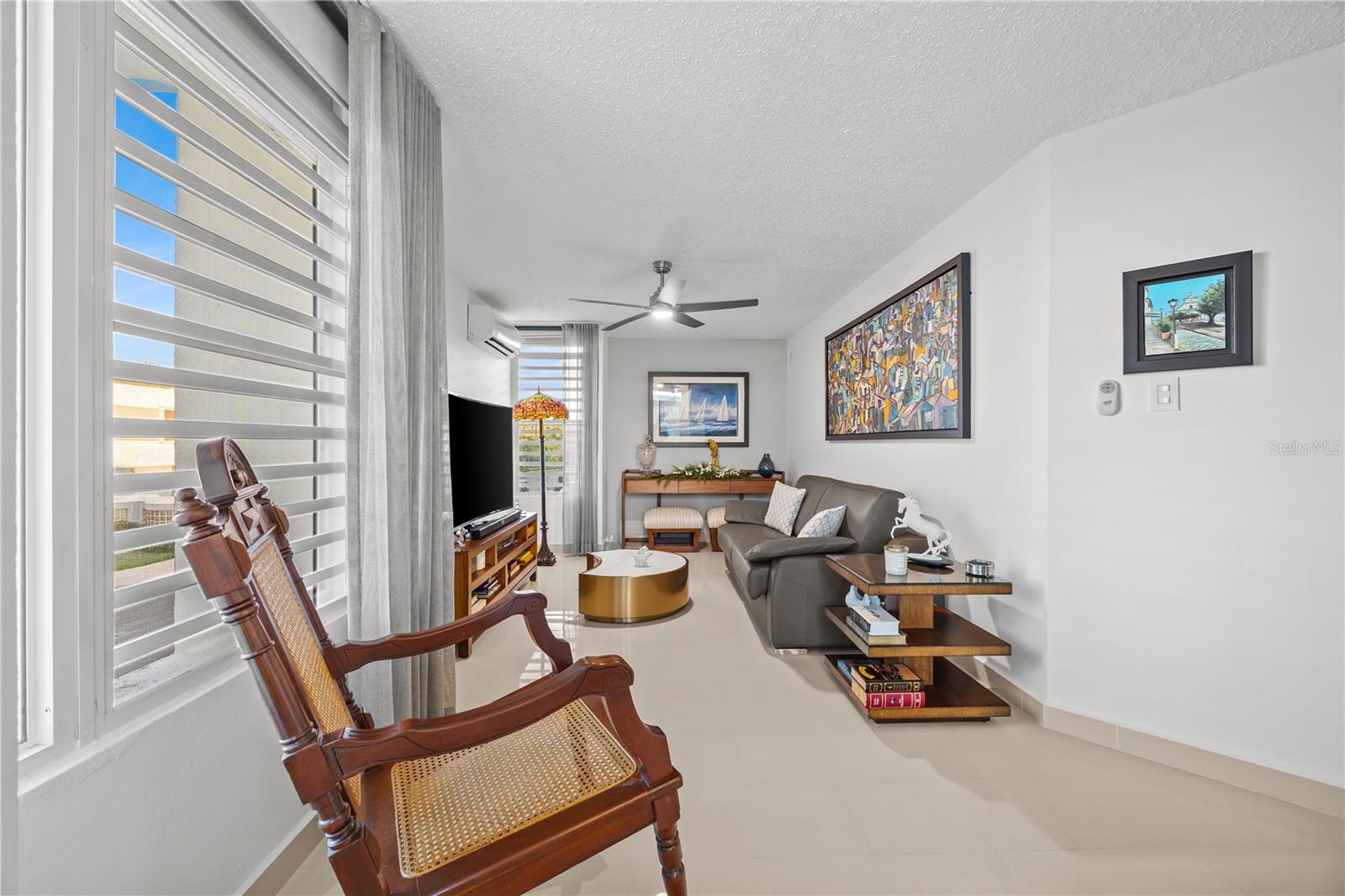 Living room with a wooden rocking chair, gray sofa, and large shuttered windows.