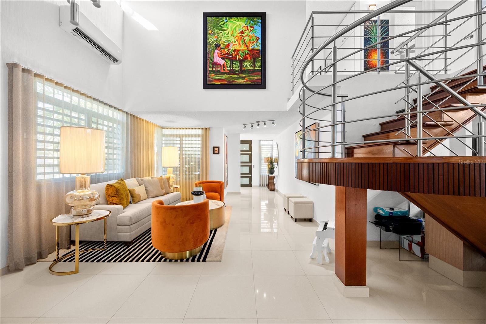 Living room with curved wood staircase, stainless-steel railings, and orange accent chairs.