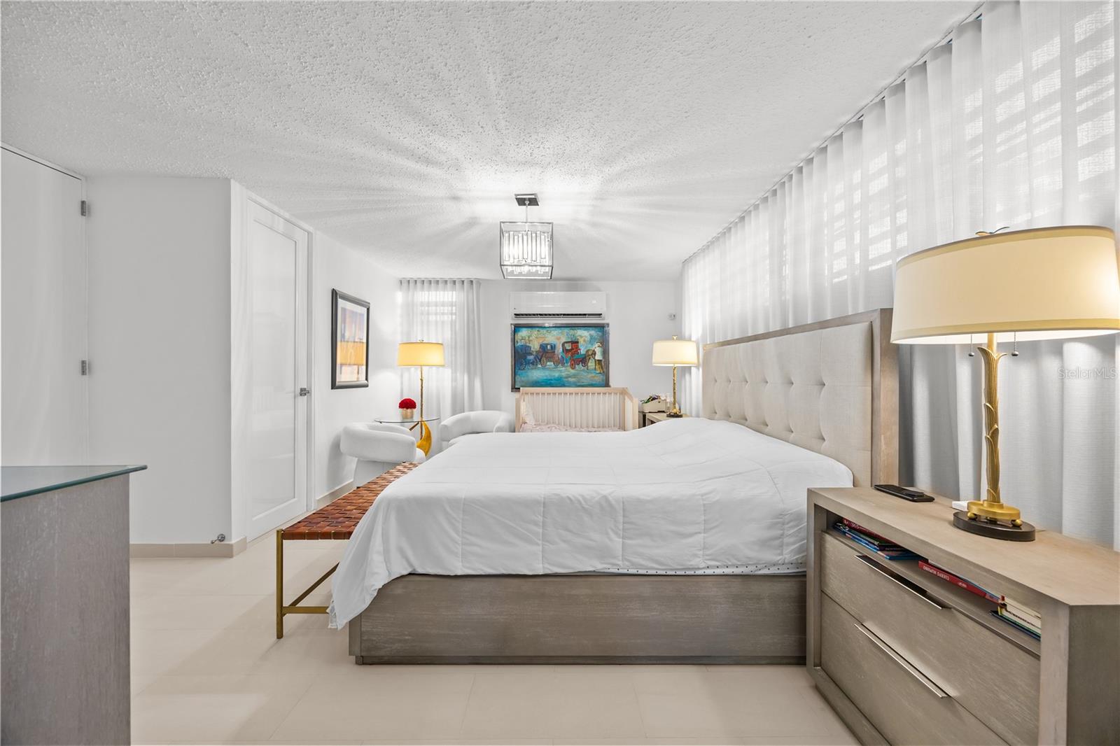 Bright bedroom with a large upholstered bed and sheer curtains along the wall.