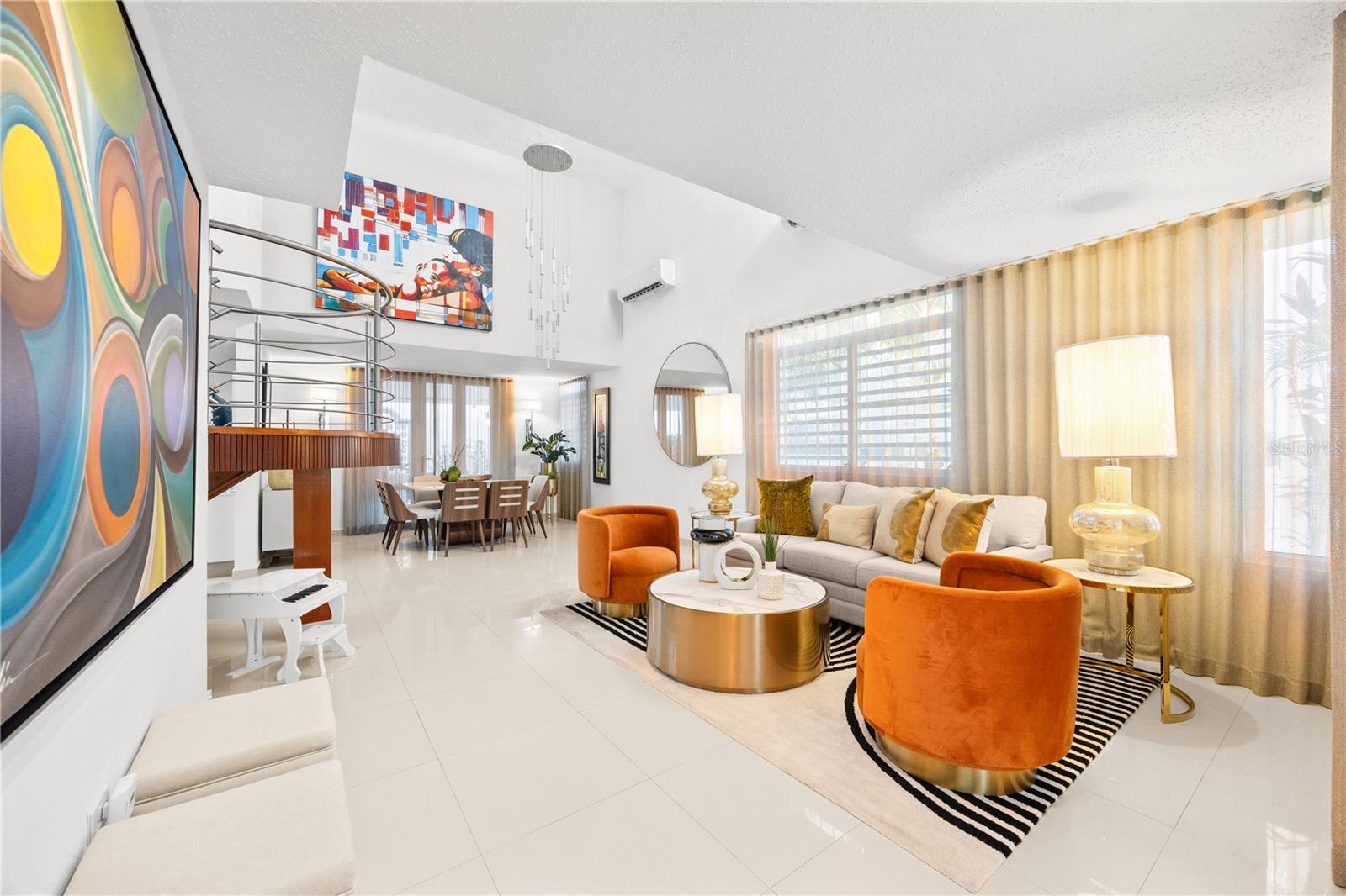 Bright living room with orange chairs, a white sofa, colorful artwork, and an open dining area.