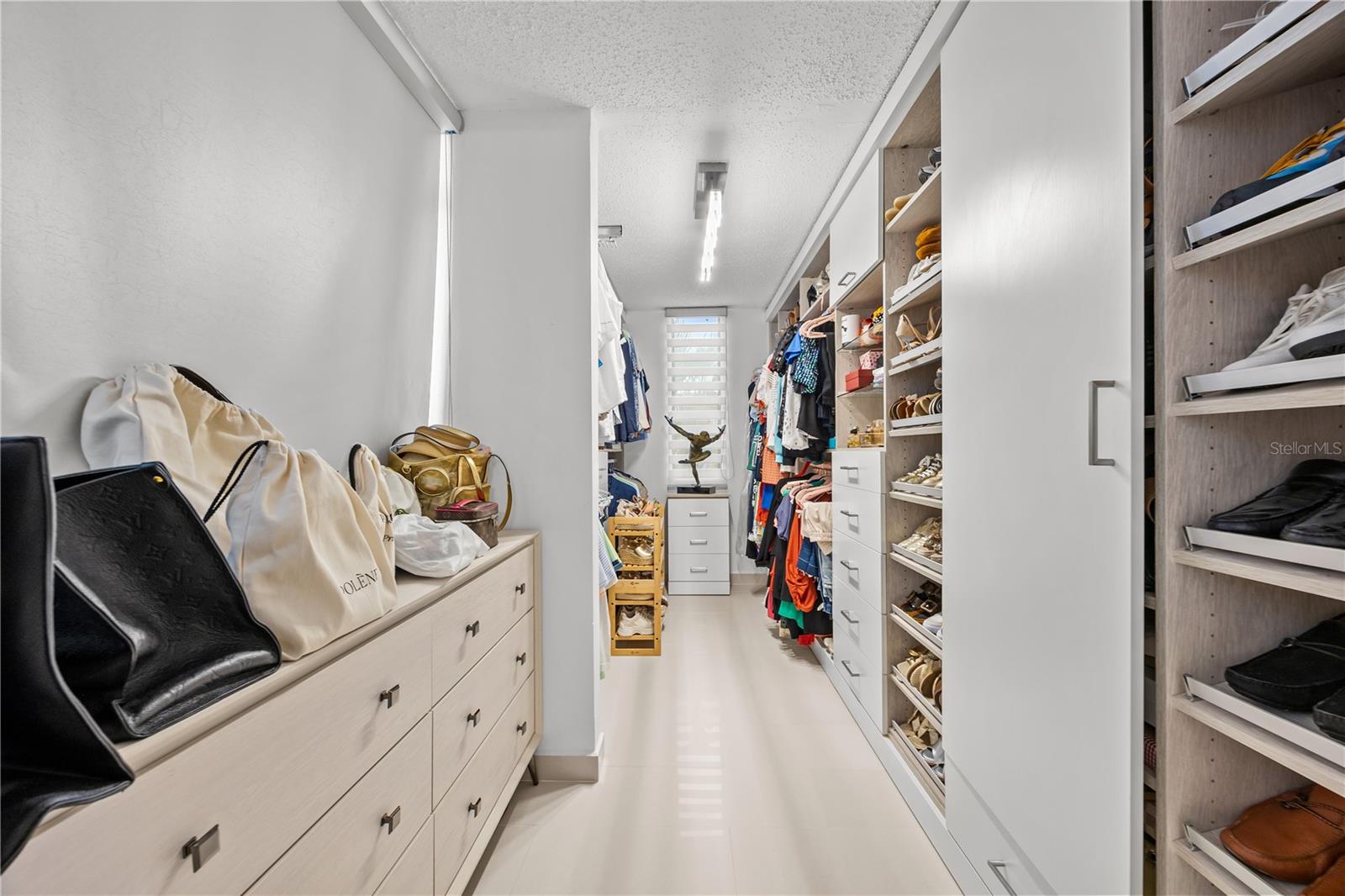 Walk-in closet with built-in shelving, shoe racks, clothing, and light wood drawers.