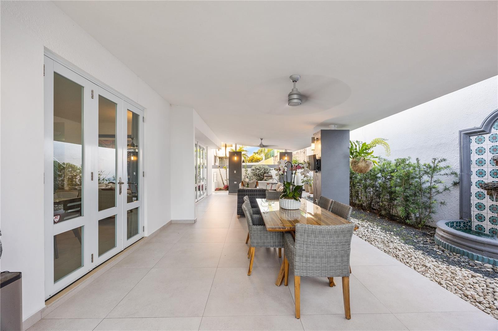 Covered patio with wicker dining set, glass doors, ceiling fans, and a tiled fountain.