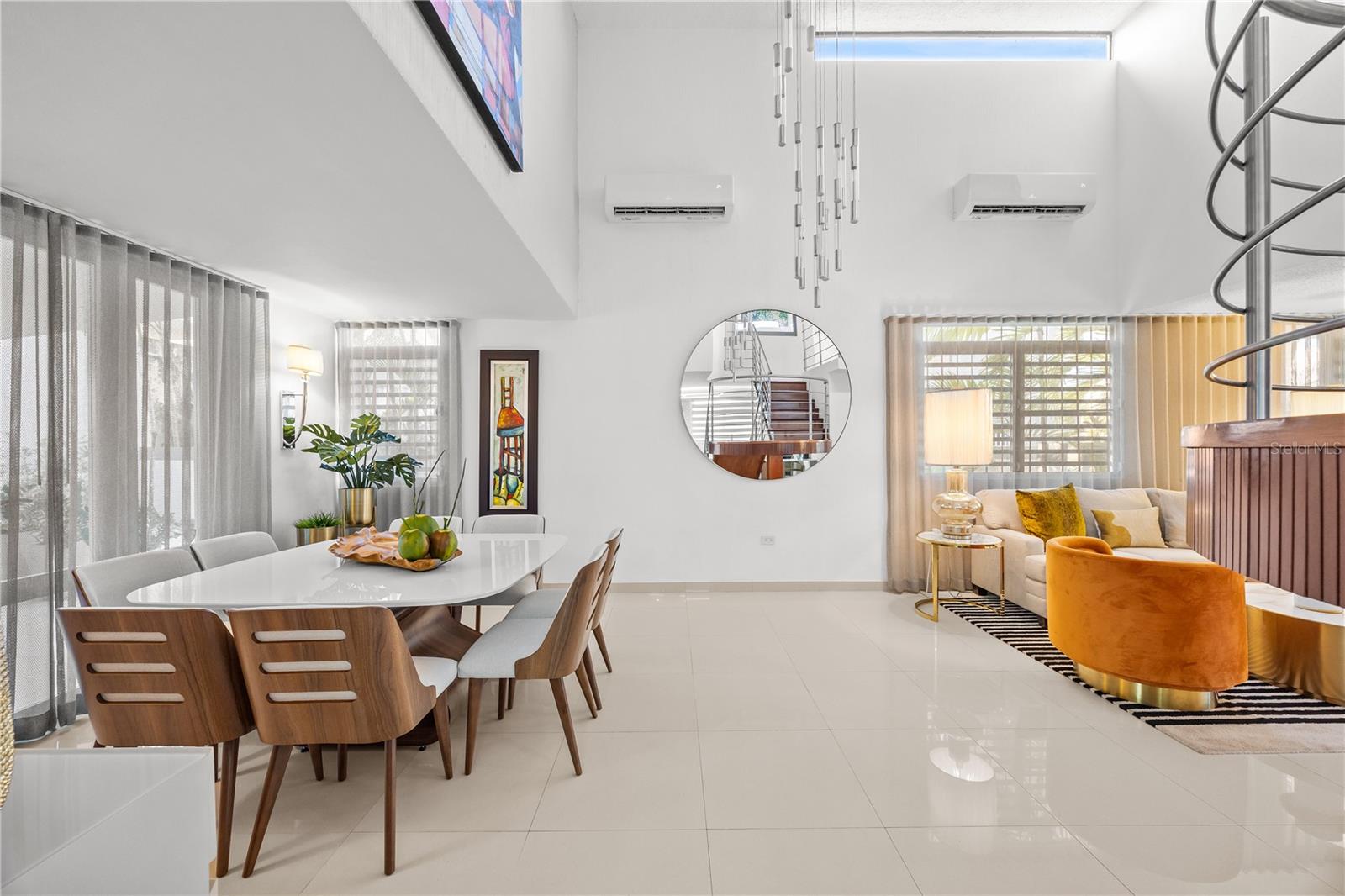 Open-plan dining and living room with a spiral staircase, high ceiling, and orange accent chair.
