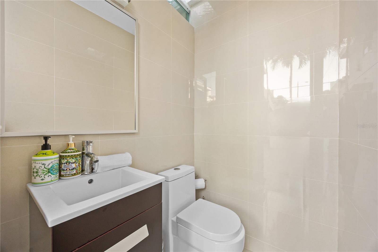 Bathroom with glossy beige tile, a dark vanity, white sink, and toilet.