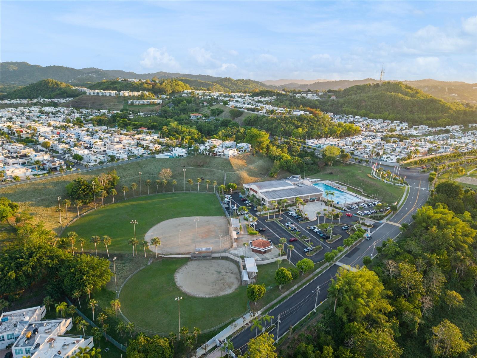 Aerial view of a hilly residential neighborhood, with baseball fields and a swimming pool in the foreground.