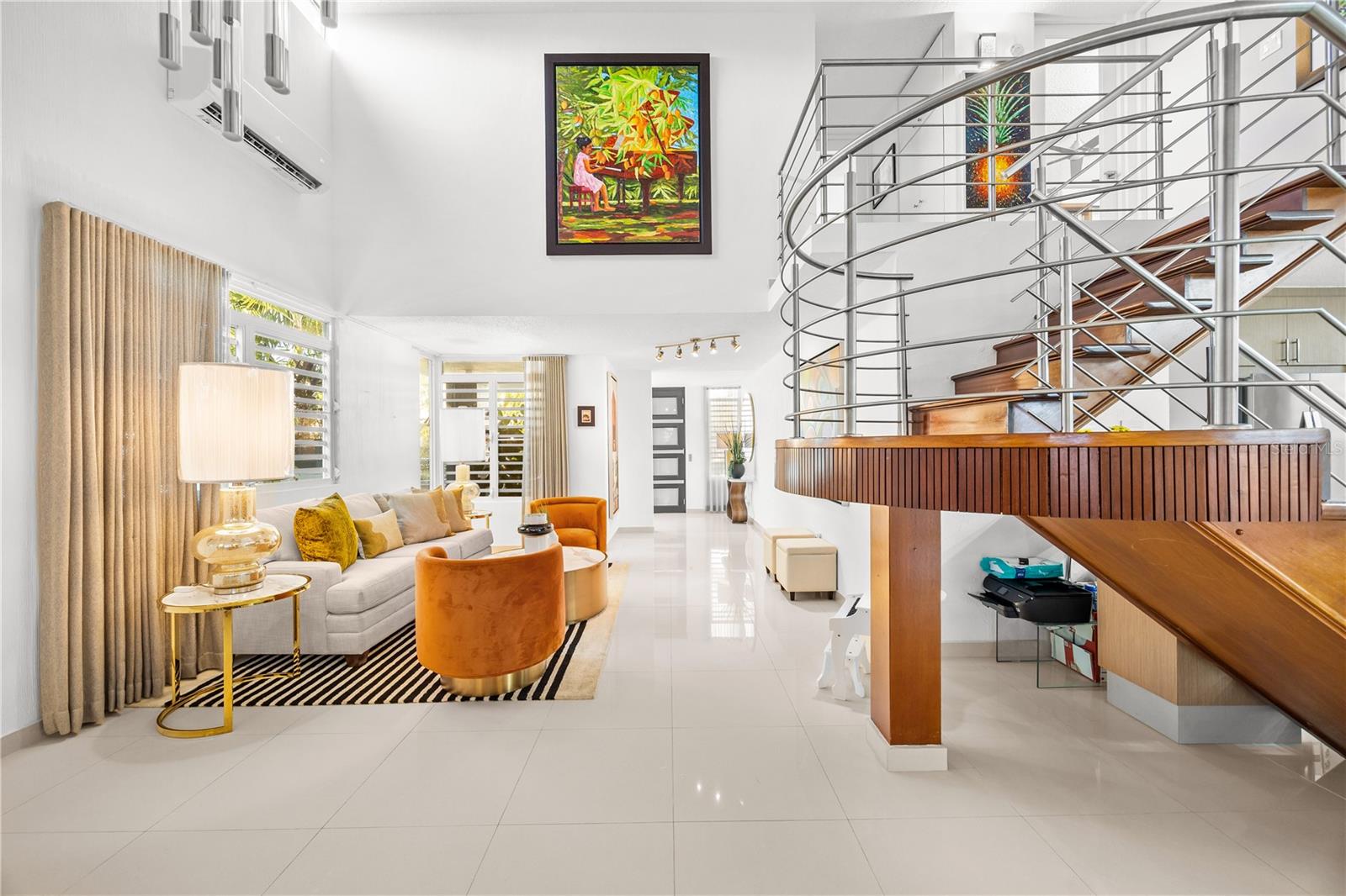 Double-height living room with a curved wood-and-metal staircase and colorful wall art.