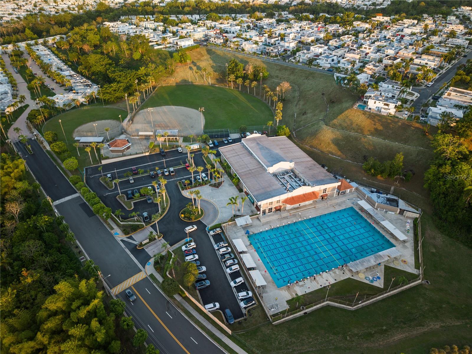 Aerial view of a community pool and sports courts surrounded by homes and green space.