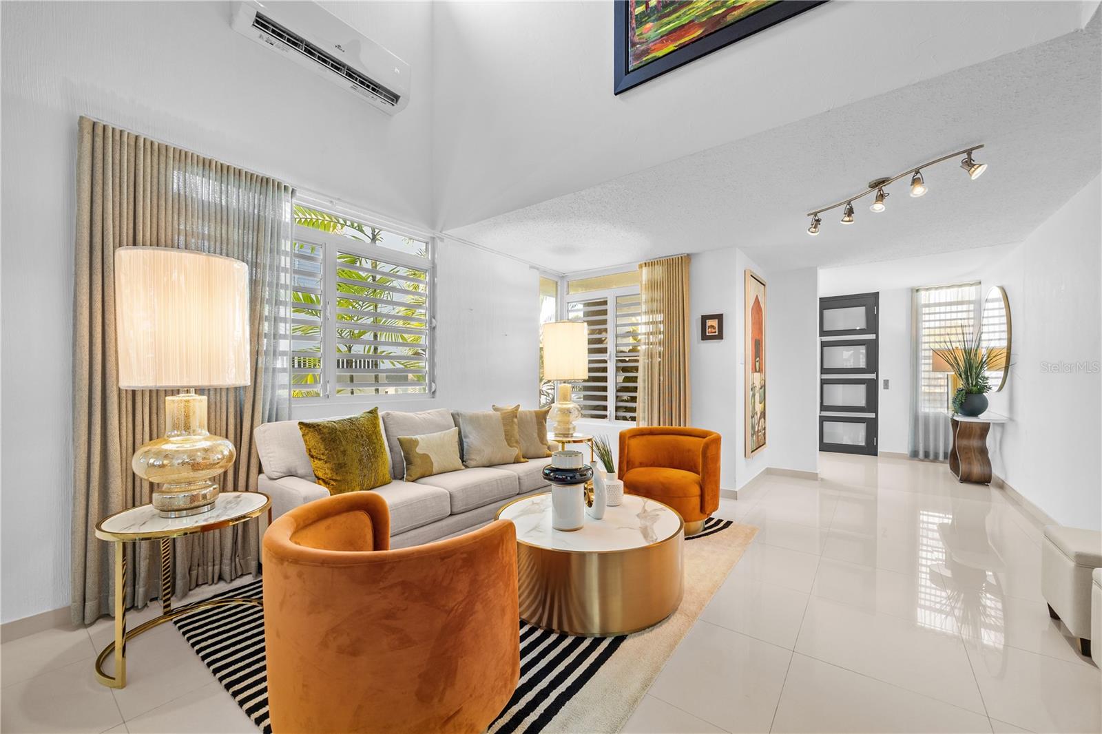 Furnished living room with orange velvet armchairs, a light sofa, and large louvered windows.