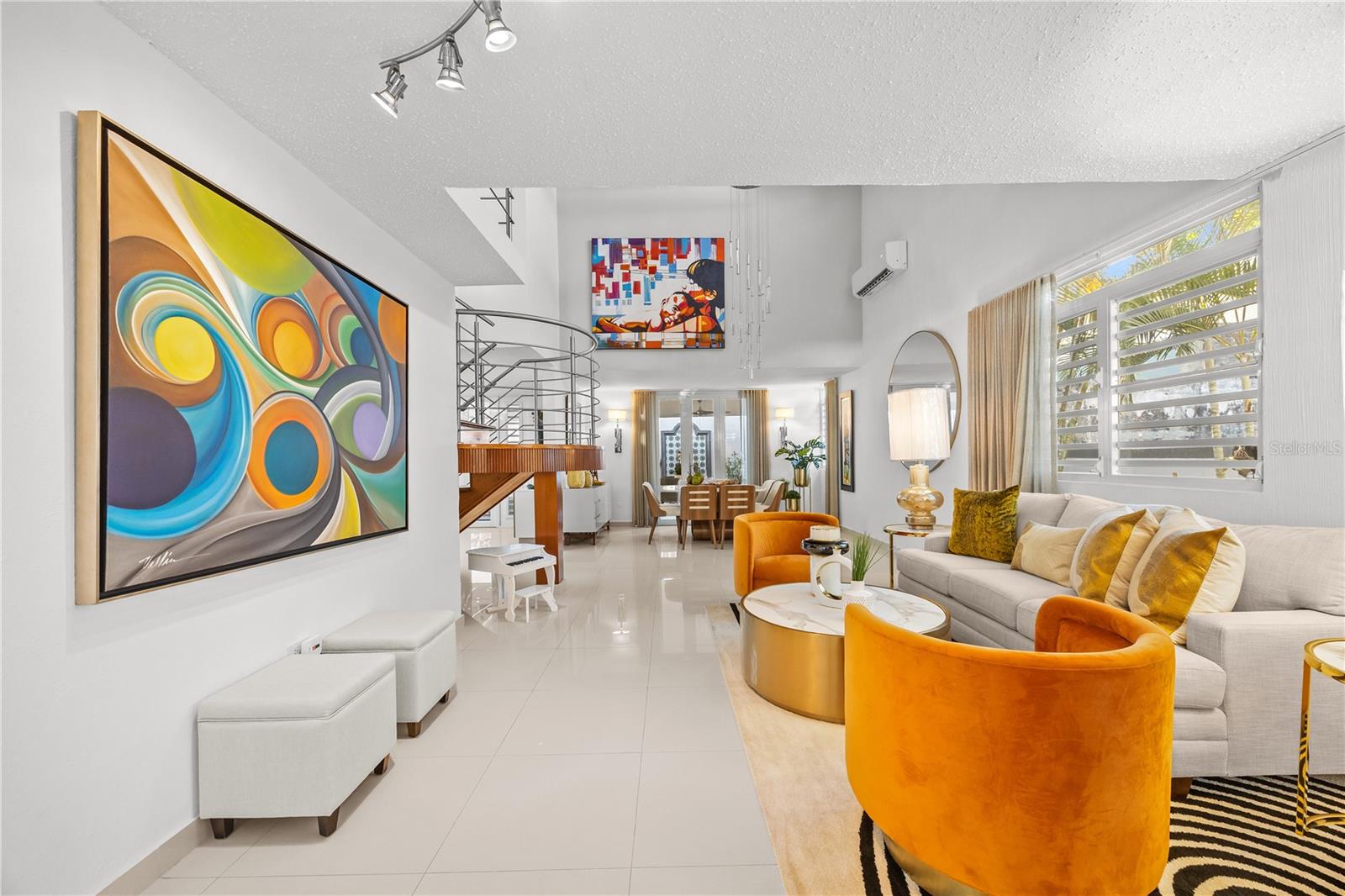 Open-plan living room with orange accent chairs, colorful artwork, and dining area beyond.