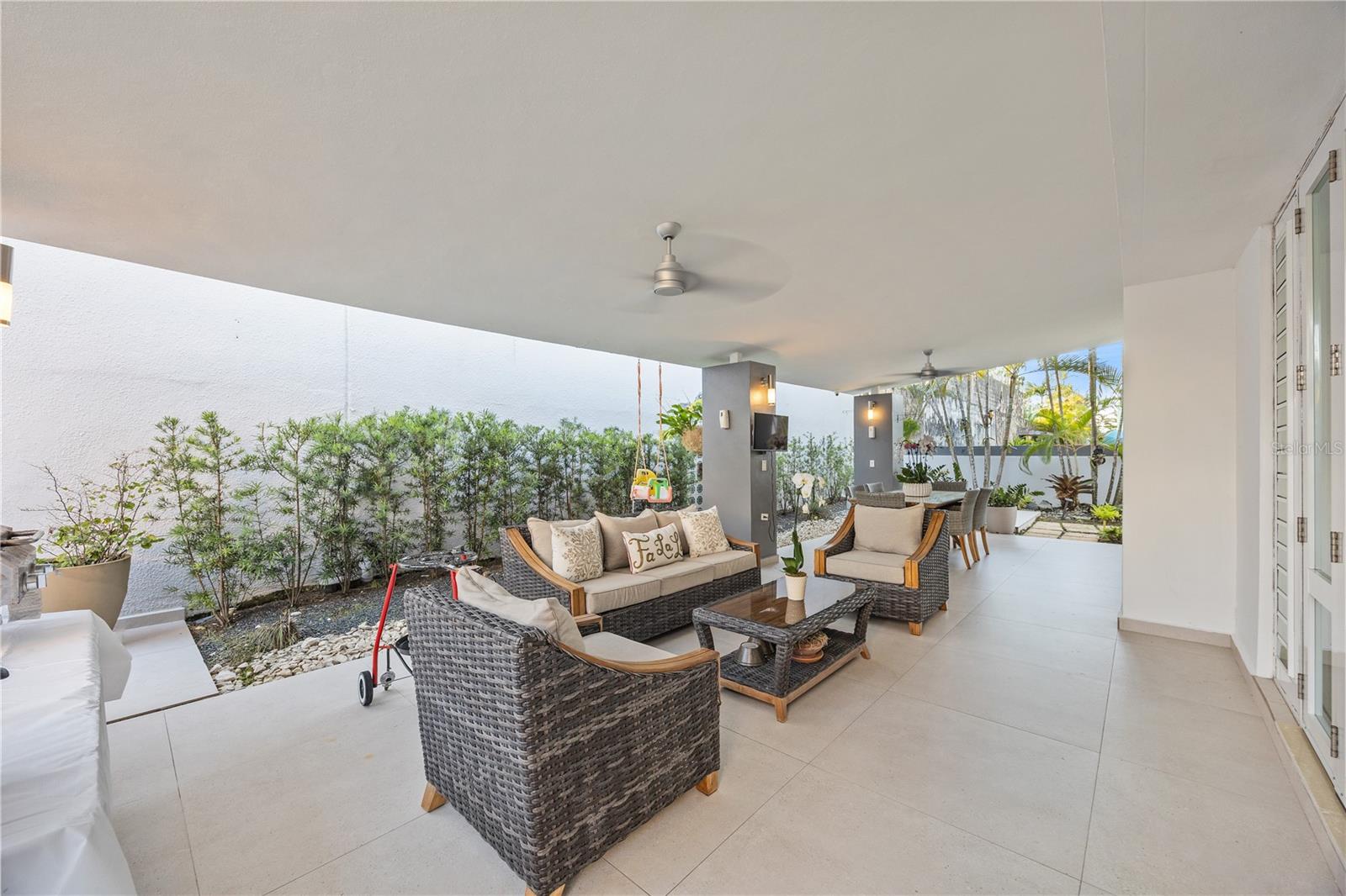 Furnished covered patio with wicker lounge seating, an outdoor dining table, and a landscaped garden.