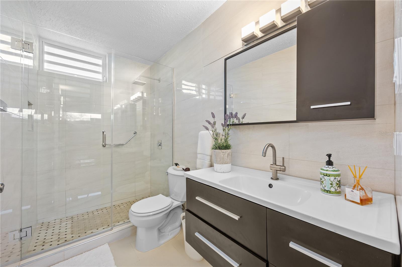 Modern bathroom with a glass walk-in shower and dark vanity with white sink.