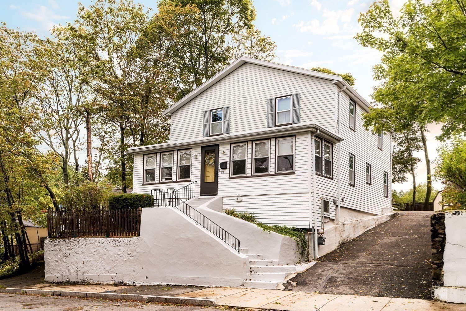 Two-story white-sided house with raised front steps, black railings, and a sloped driveway.