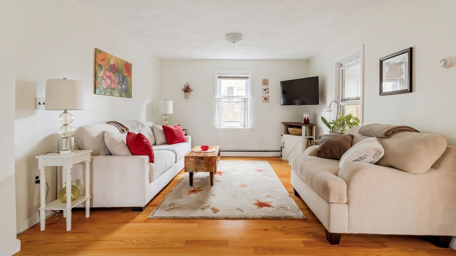 Living room with cream sofas, red pillows, a wooden coffee table, and a floral rug.