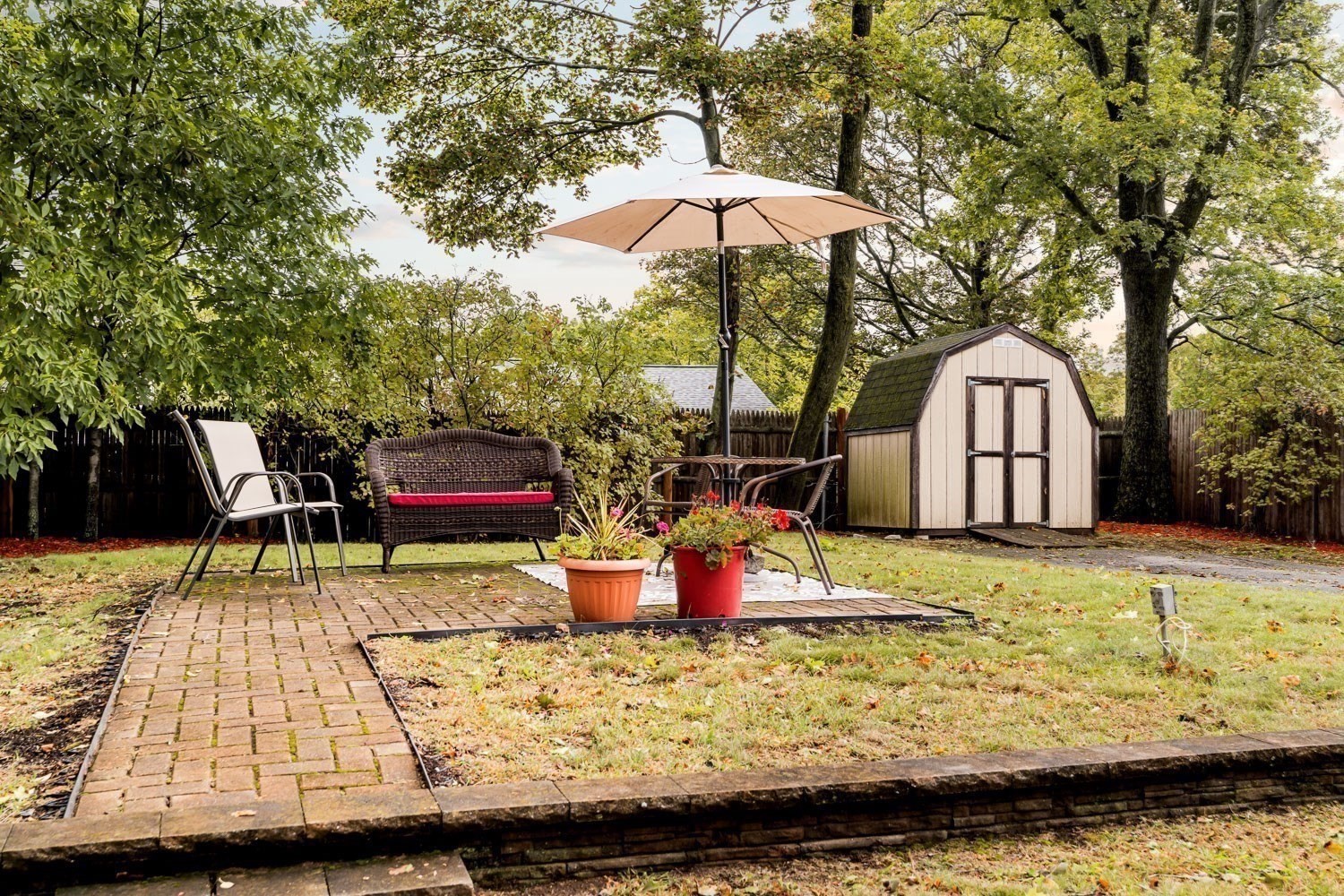 Backyard patio with outdoor seating beneath an umbrella, potted flowers, and a garden shed.
