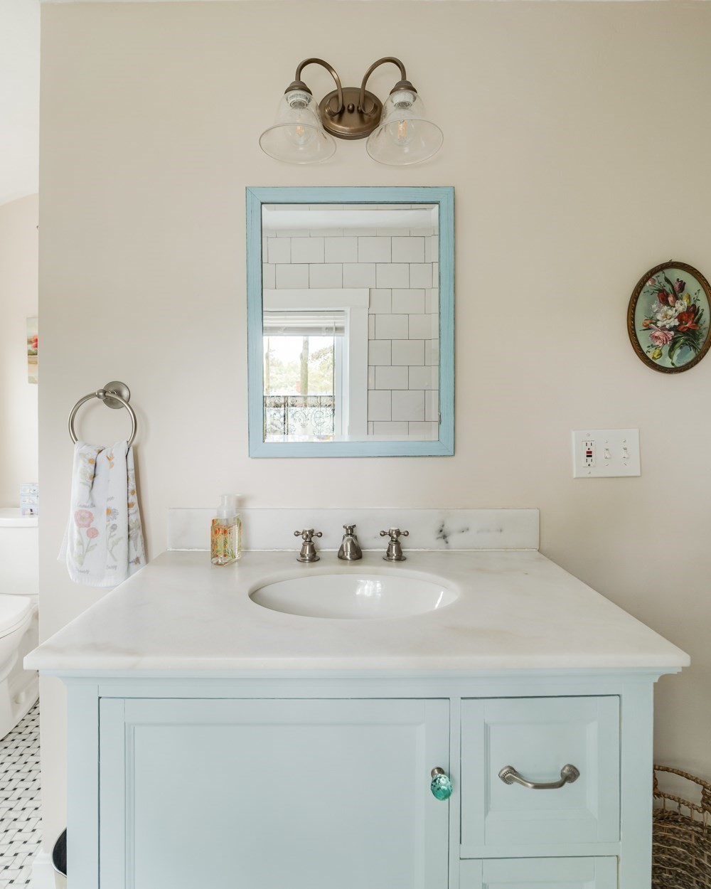 Bathroom vanity with pale blue cabinetry, marble counter, oval sink, and blue-framed mirror.