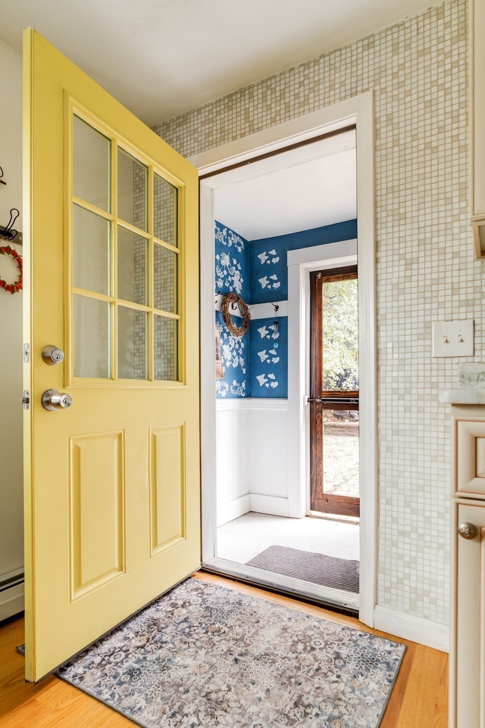 Entryway with a yellow glass-paneled door, tiled walls, and a view into a blue floral-papered room.