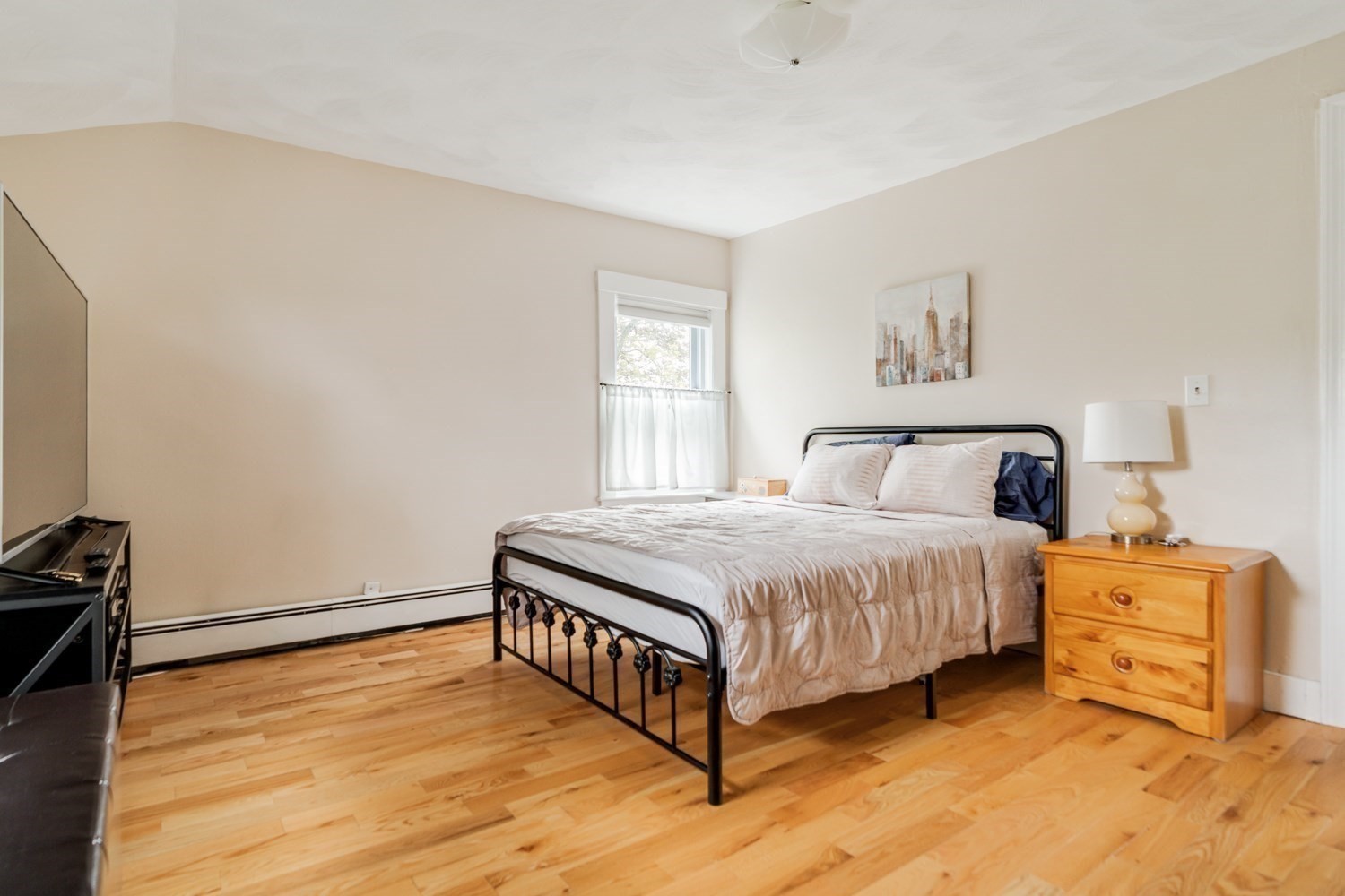 Bedroom with a black metal bed, light bedding, hardwood floors, and a wooden nightstand.