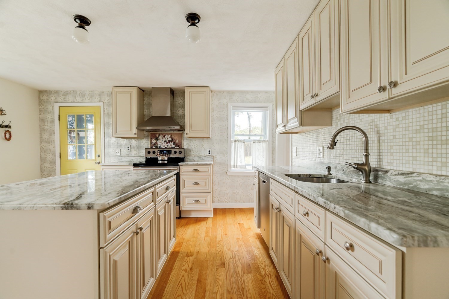 Kitchen with cream cabinets, marble-pattern counters, a large island, mosaic tile backsplash, and hardwood floors.