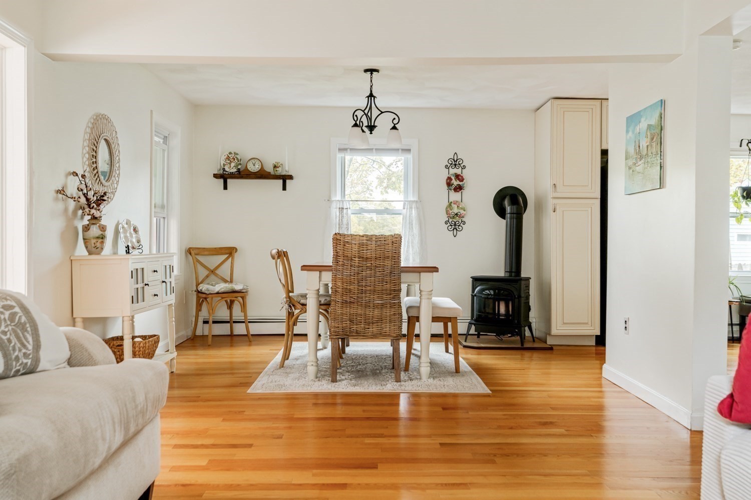 Dining area with a wooden table, hardwood floors, and a black wood stove beside the living room.