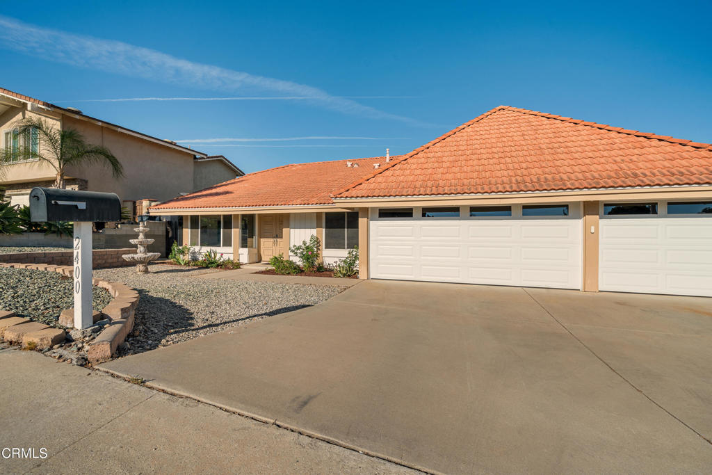 Single-story home with terracotta tile roof, two white garage doors, and gravel front yard.