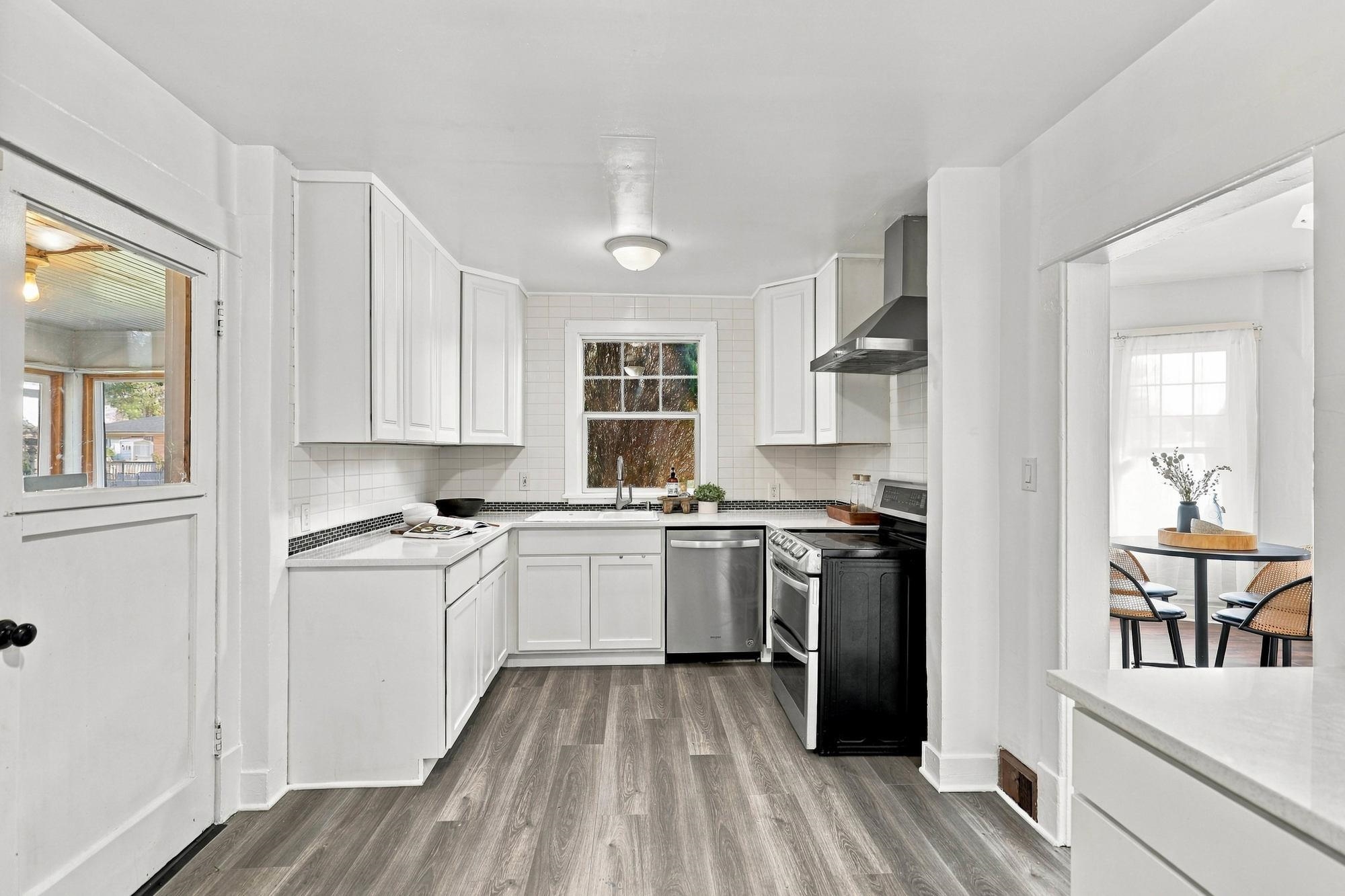 Bright white kitchen with stainless appliances and a dining nook visible through the doorway.