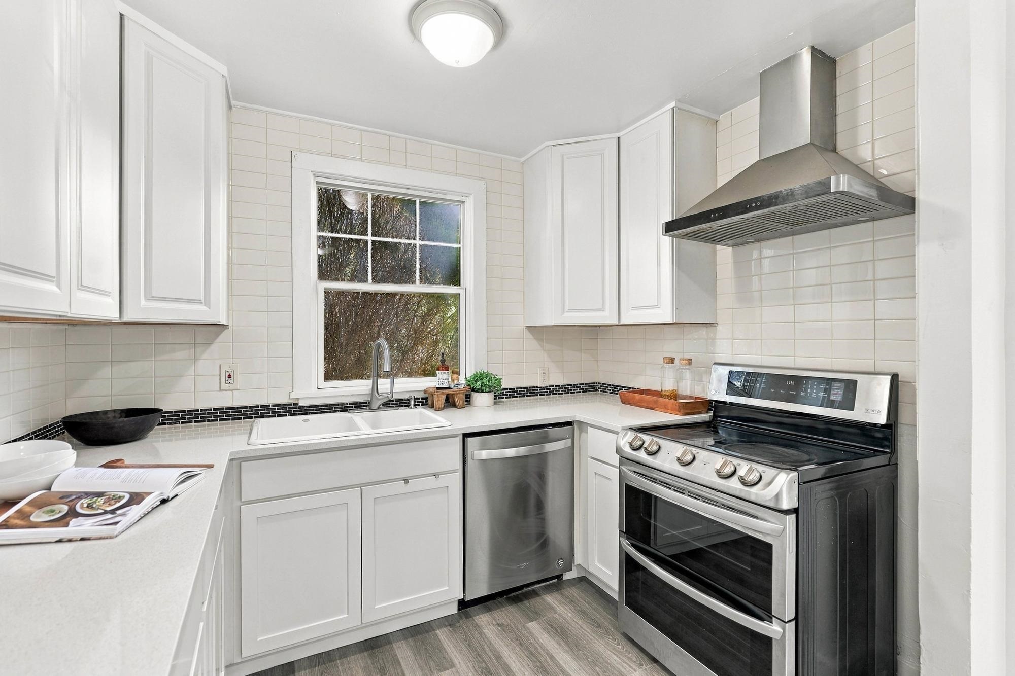 Kitchen with white cabinets, tiled backsplash, window over the sink, and stainless steel appliances.