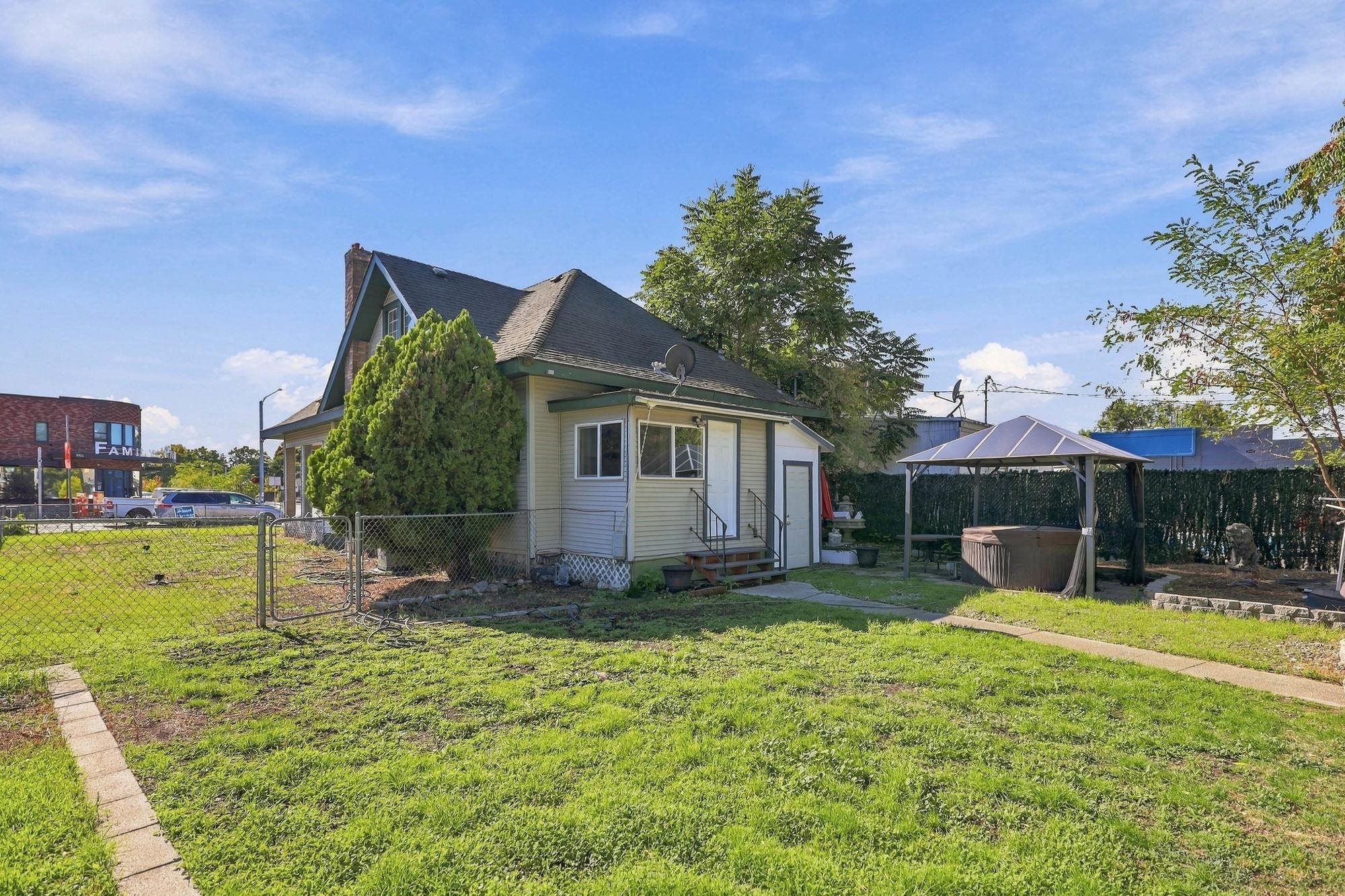 House and grassy backyard with chain-link fencing and a covered hot tub.