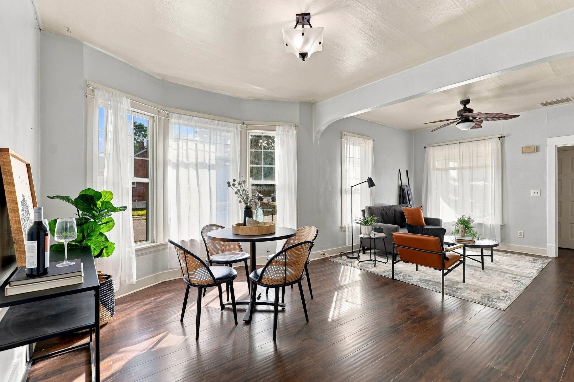 Living and dining room with large curtained windows, dark hardwood floors, and a ceiling fan.