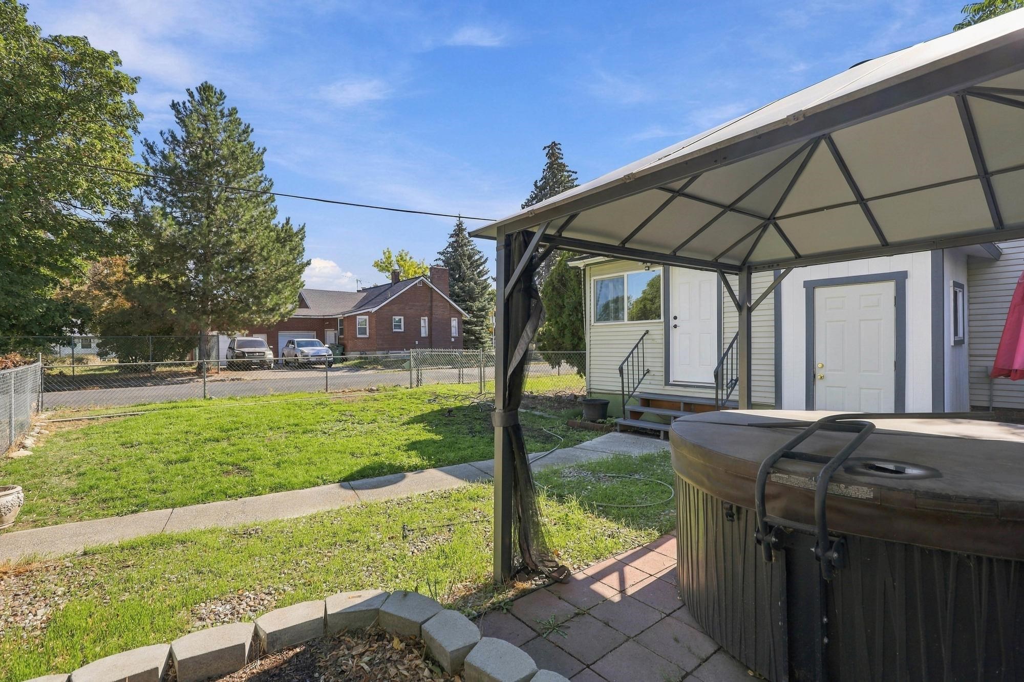 Backyard patio with a covered hot tub, lawn, and fenced yard.