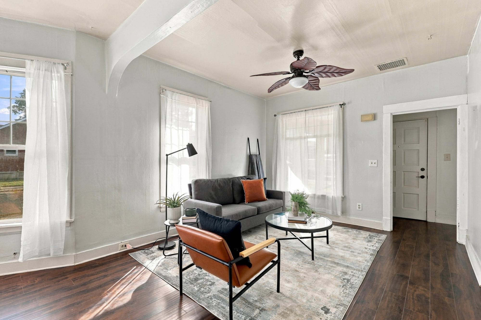 Furnished living room with a gray sofa, leather chair, large windows, and dark wood floors.