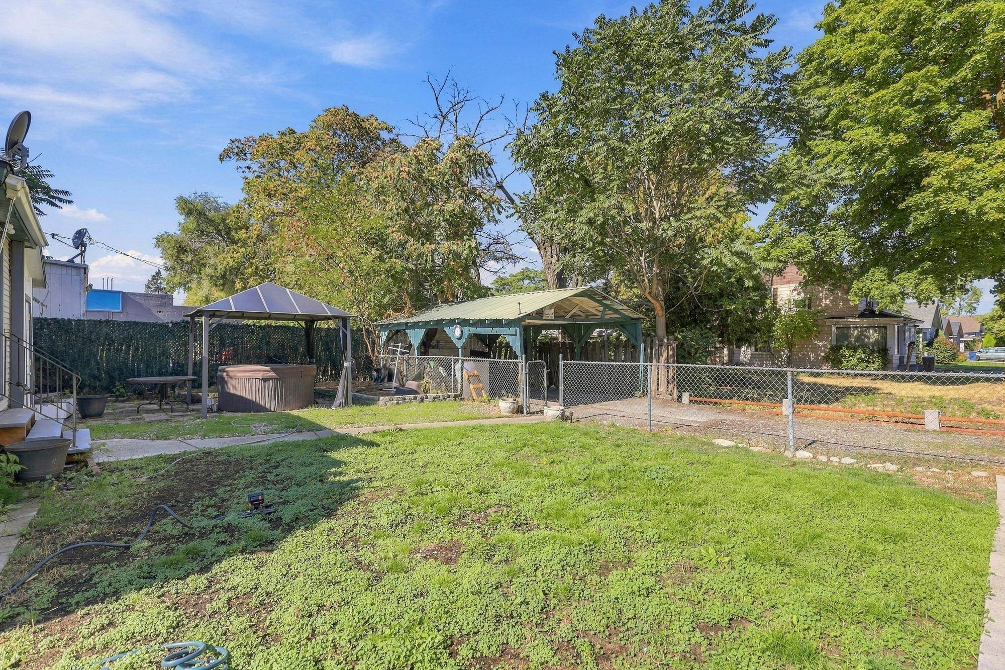 Backyard with a hot tub, covered patio, mature trees, and fenced lawn.
