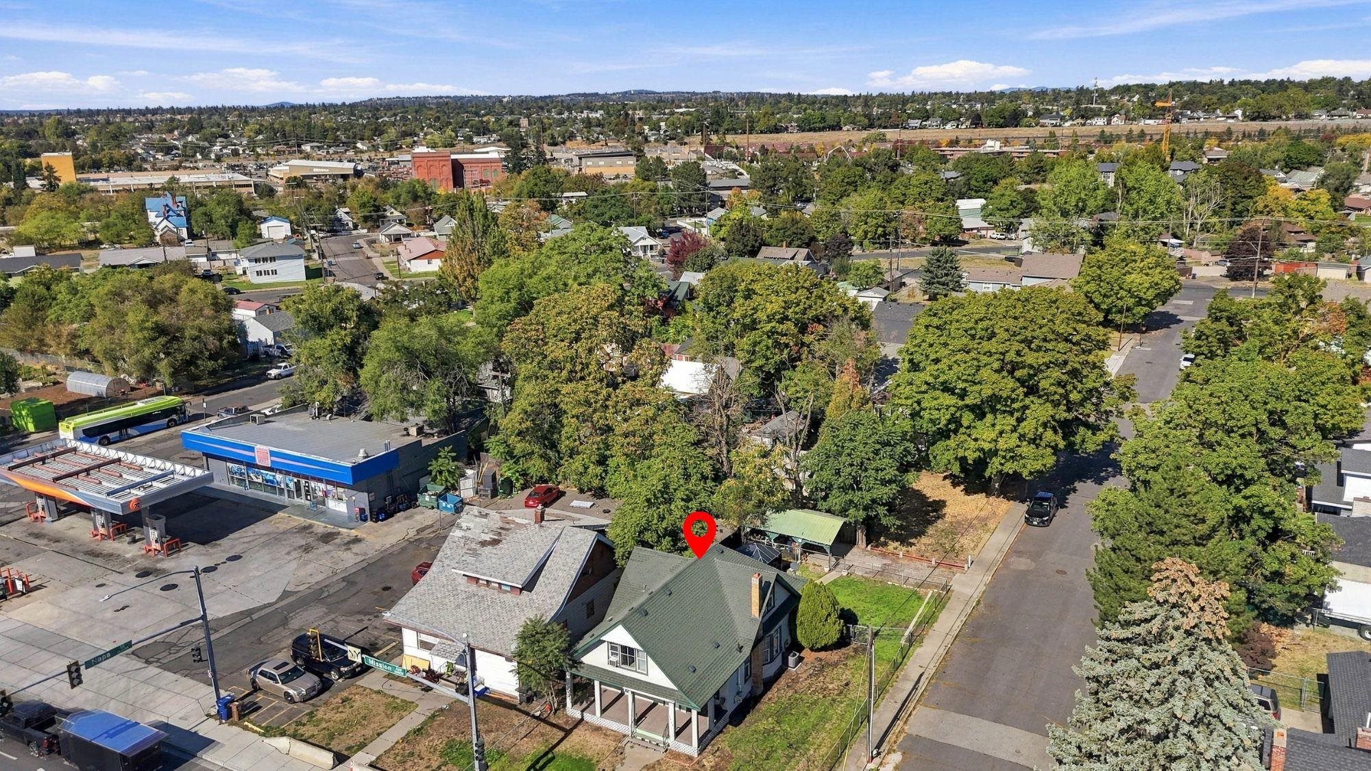 Aerial view of a green-roofed house marked near a Spokane intersection, with neighborhood homes and businesses beyond.