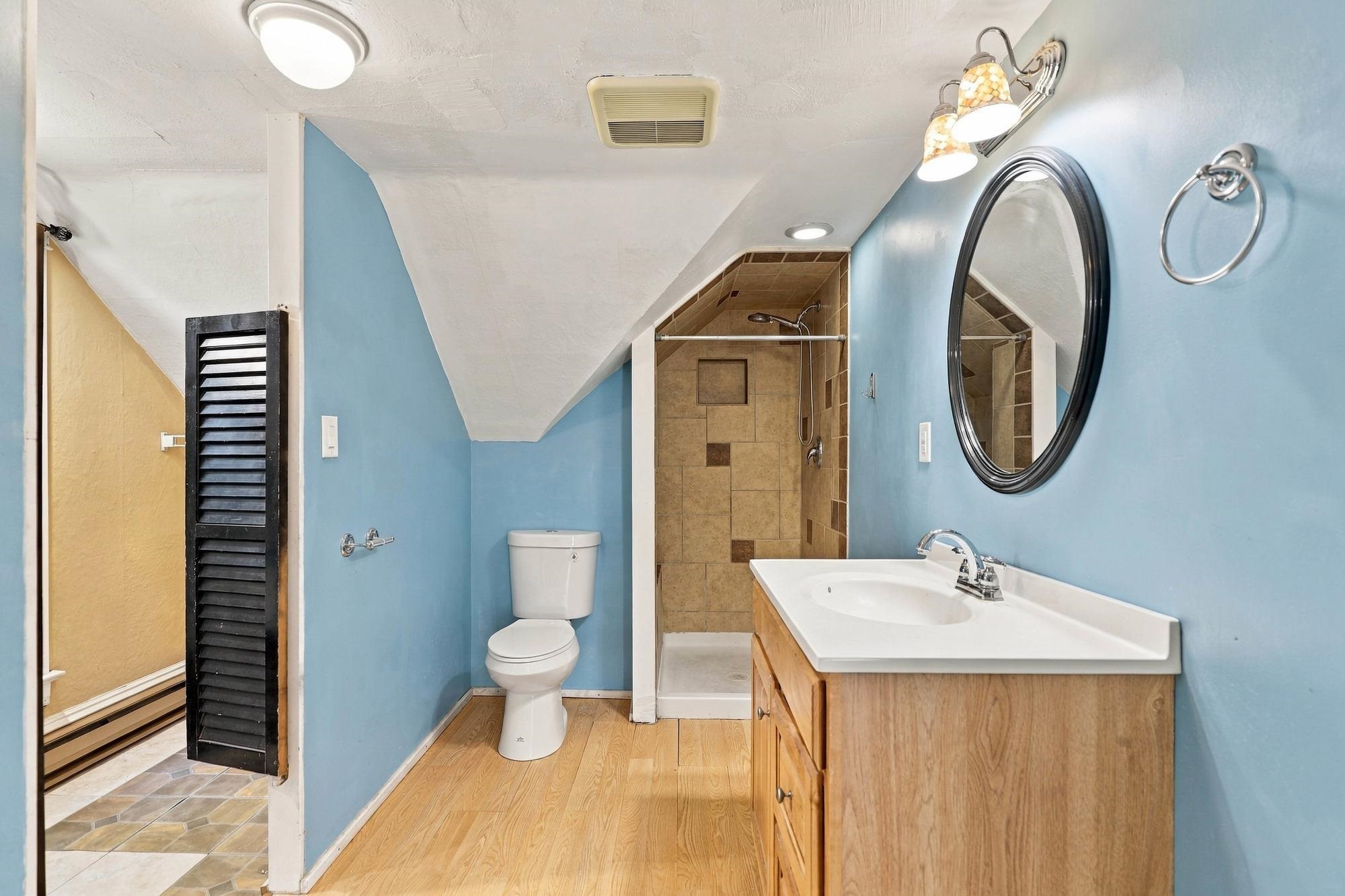 Bathroom with blue walls, a wood vanity, and a tan tiled walk-in shower beneath a sloped ceiling.