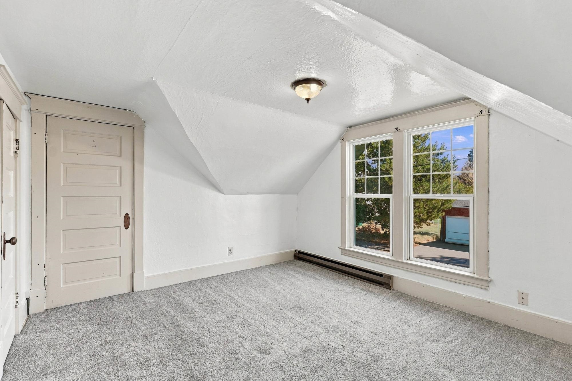 Empty bedroom with gray carpet, a sloped ceiling, and two windows.