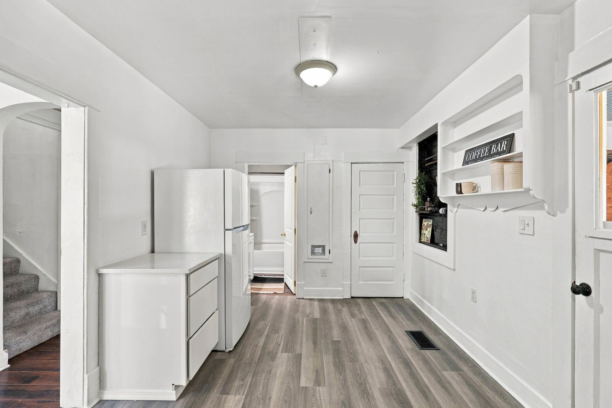 Kitchen with a white refrigerator, built-in coffee bar, gray flooring, and carpeted stairs.