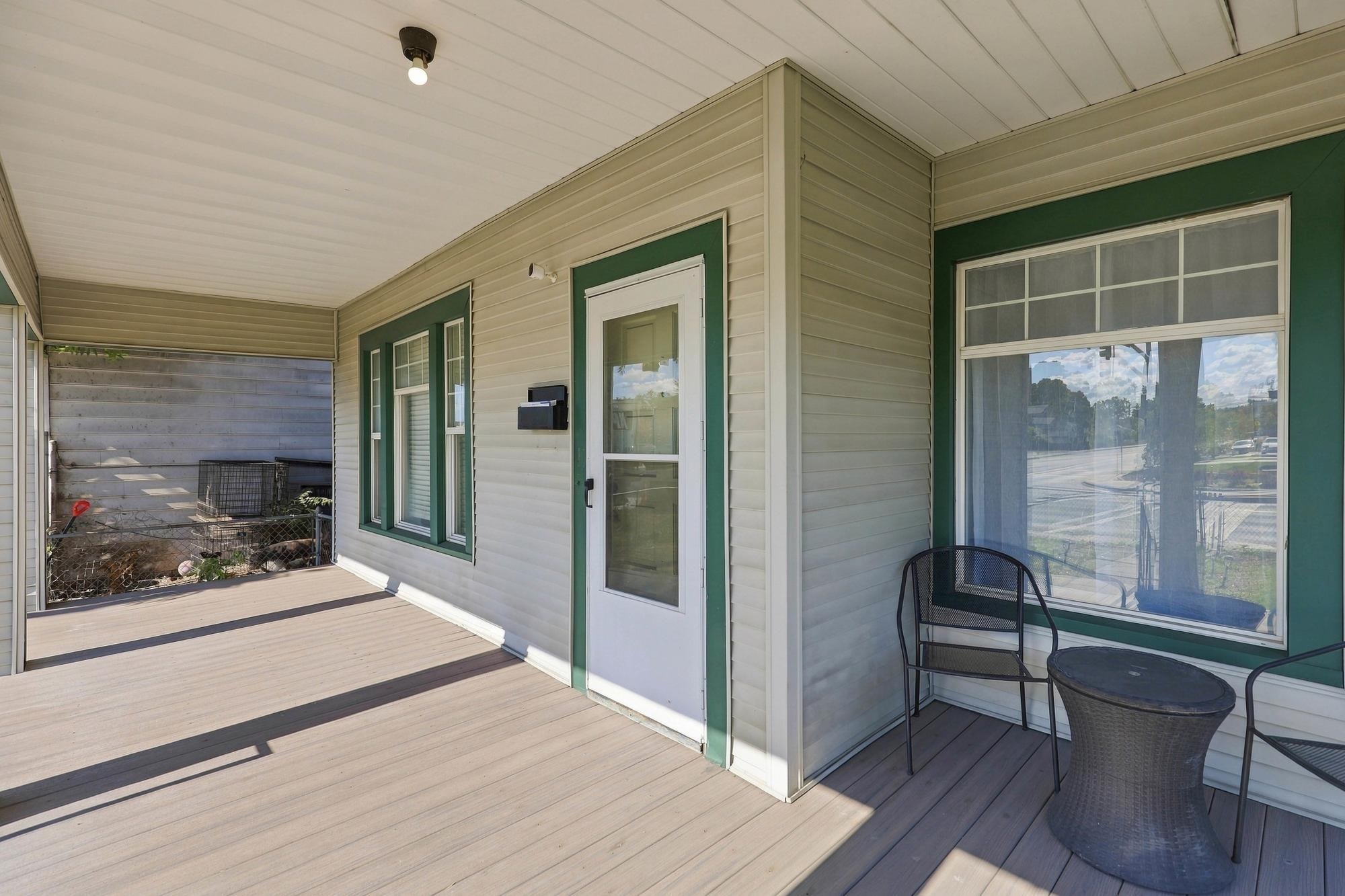 Covered porch with green-trimmed windows, a screen door, and black patio seating on a spacious deck.