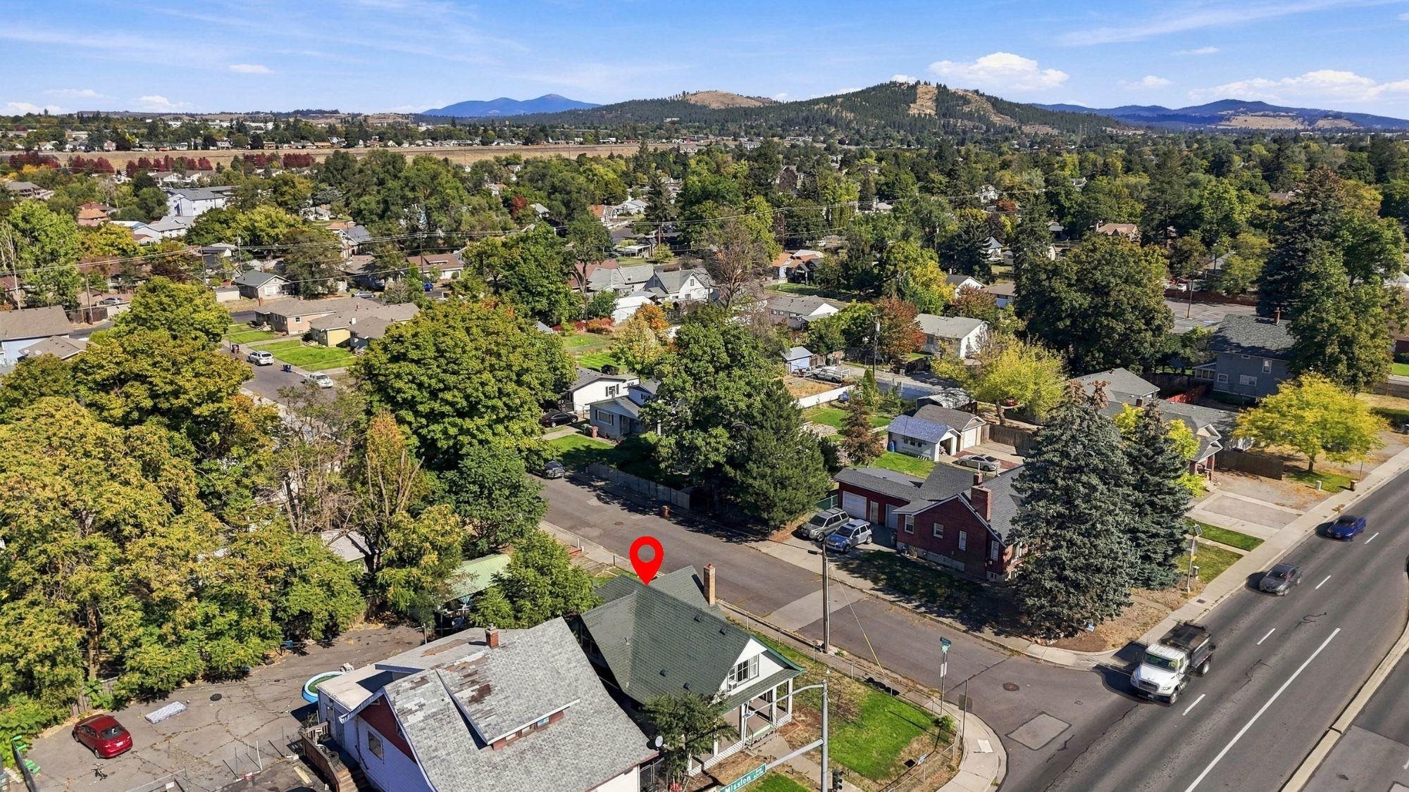 Aerial view of the property and leafy neighborhood, with wooded hills and mountains in the distance.