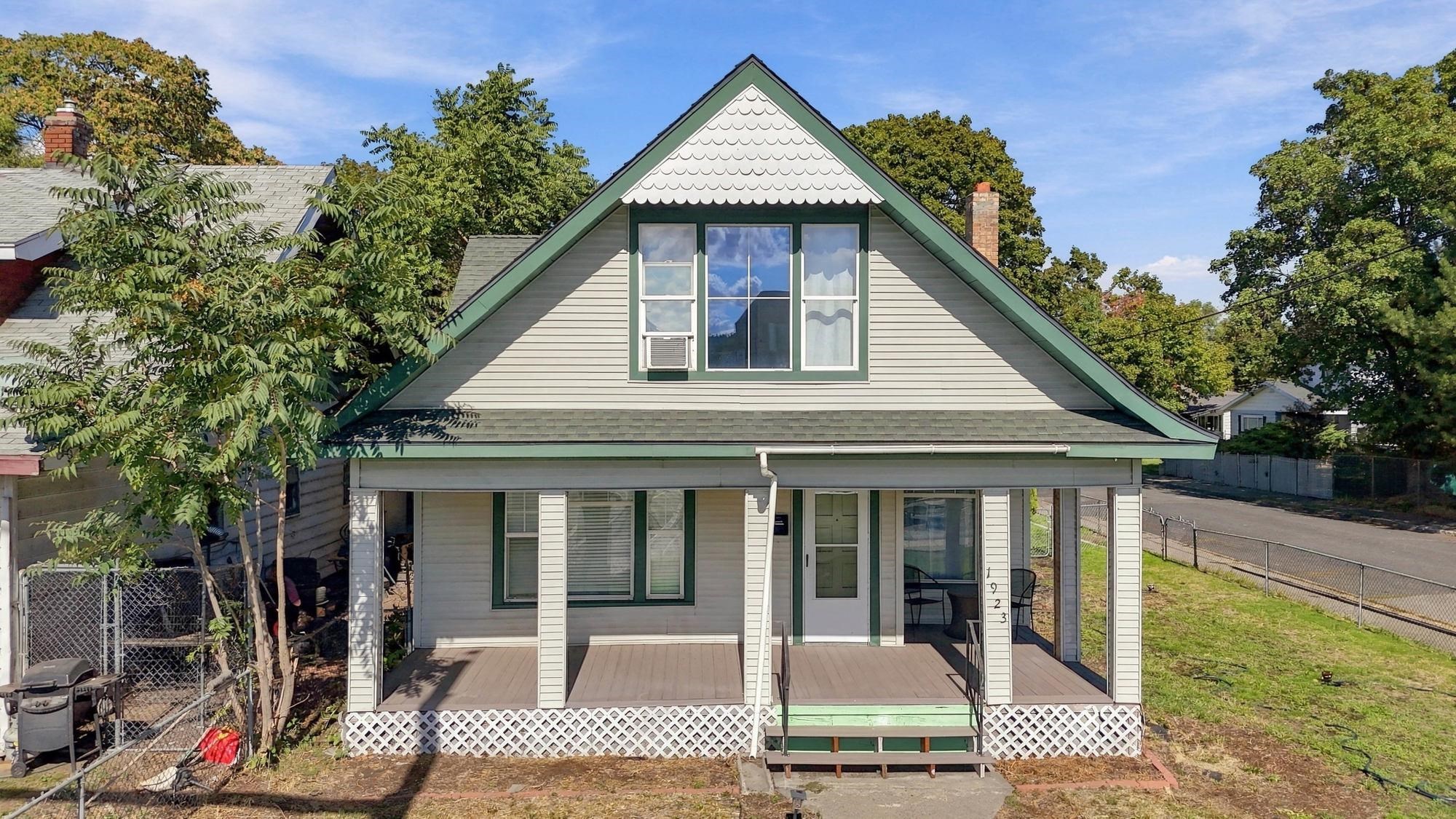 House with a steep front gable, green trim, and a covered porch behind a fenced yard.
