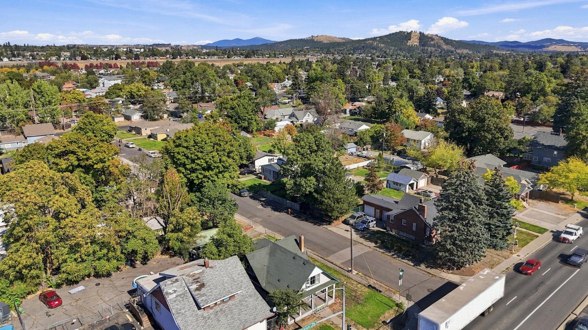 Aerial view of a leafy neighborhood with homes, streets, and distant wooded hills.