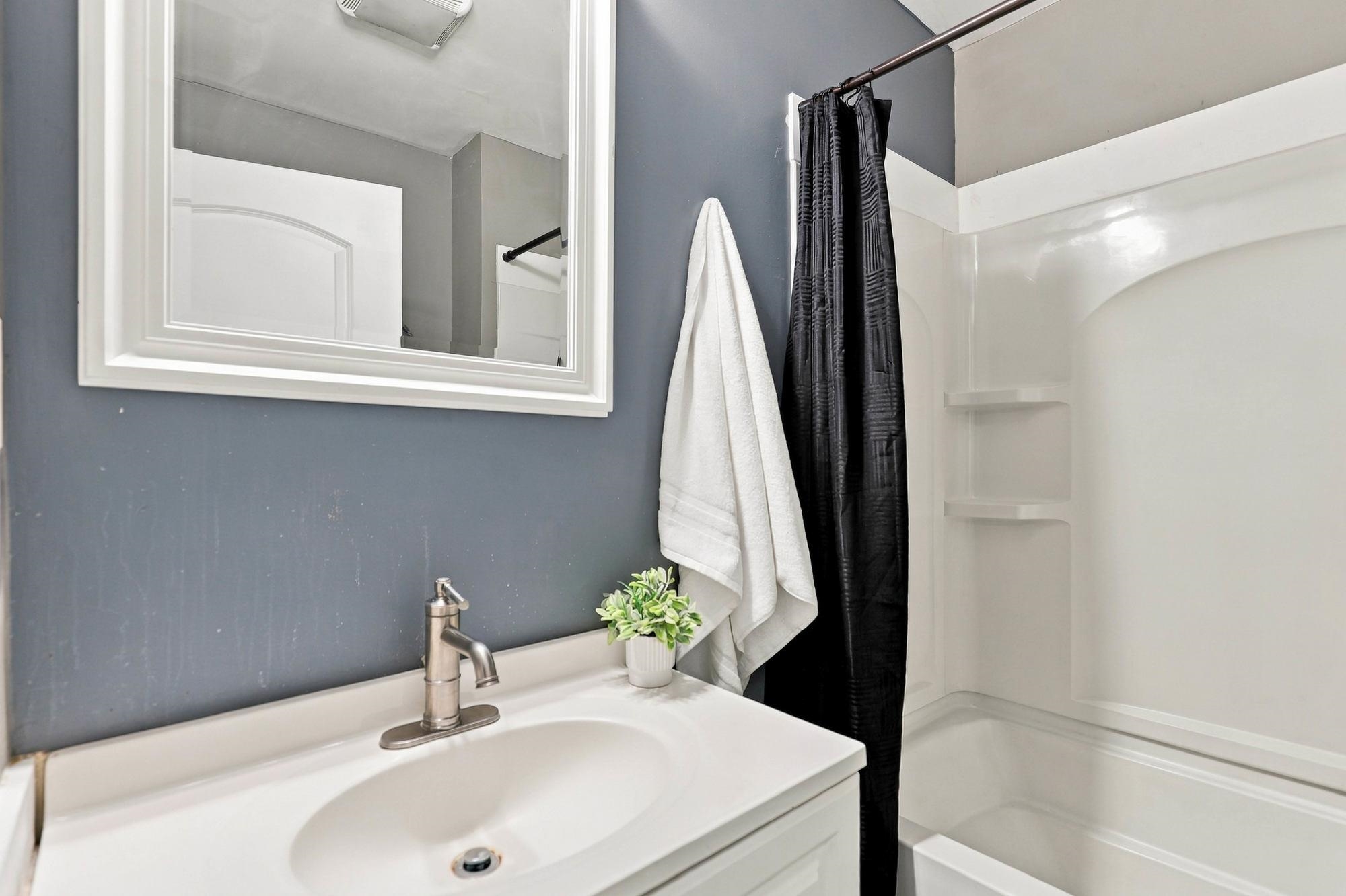 Bathroom with a white vanity, gray walls, and a tub-shower behind a black curtain.