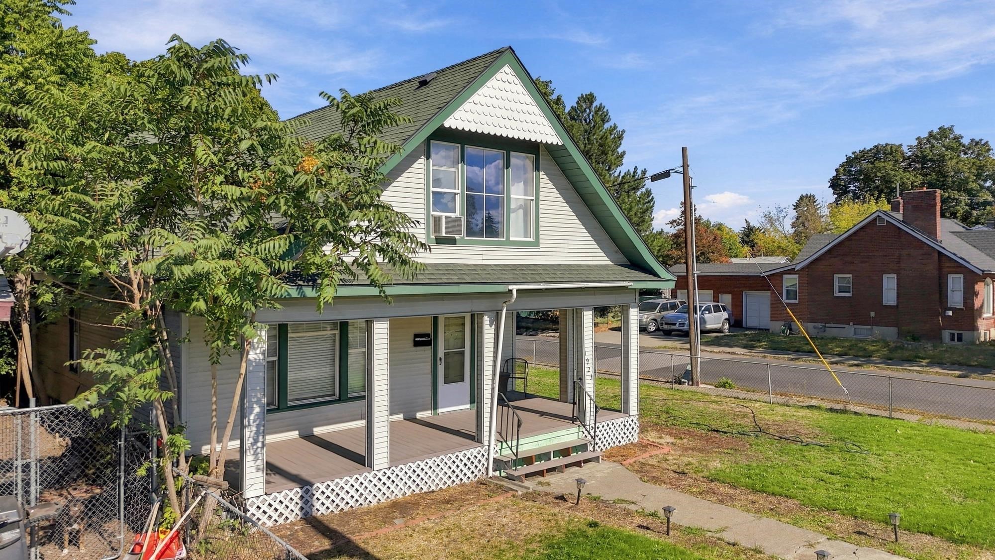 White house with green trim, a steep A-frame roof, and a covered front porch.