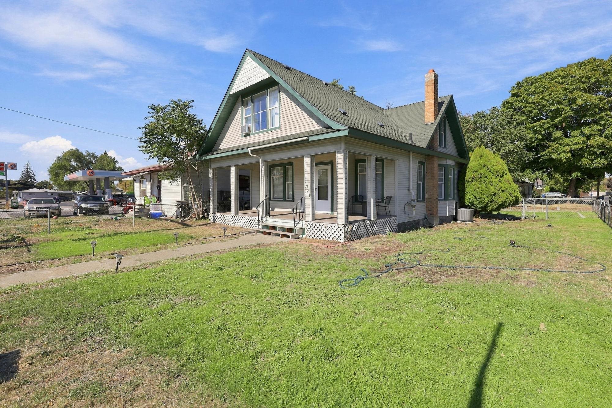 House with green-trimmed gables, a covered front porch, and a brick chimney beside a 76 gas station.